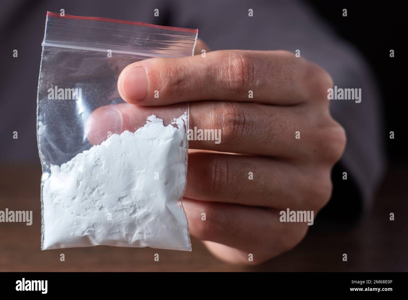 Concetto di tossicodipendenza. La mano dell'uomo tiene il pacchetto o il sacchetto di plastica con la cocaina o altre droghe, l'abuso della droga e il concetto di dipendenza di pericolo. Foto Stock