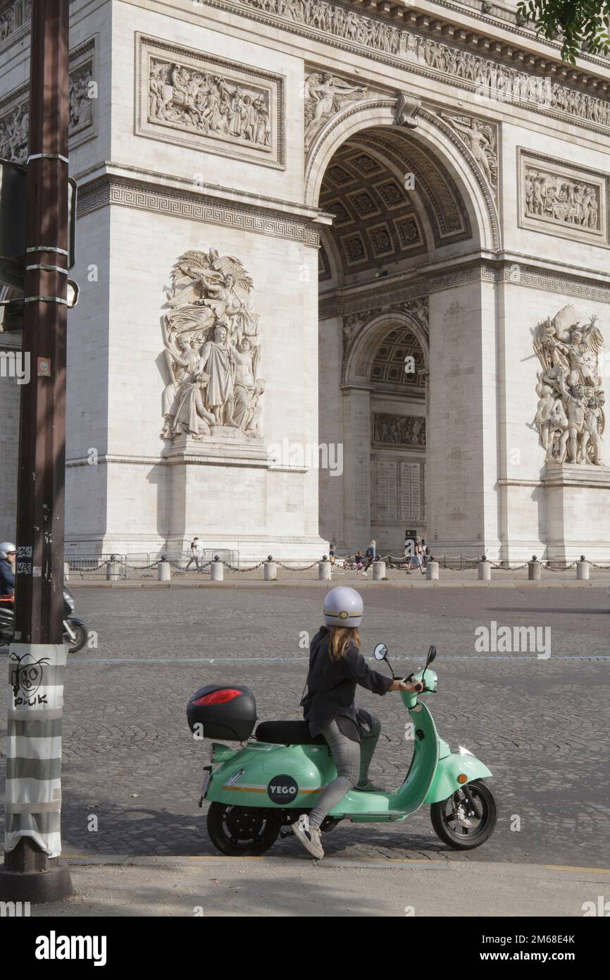 Una giovane donna in sella a uno scooter elettrico Yego noleggiato di fronte all'Arco di Trionfo a Parigi Foto Stock