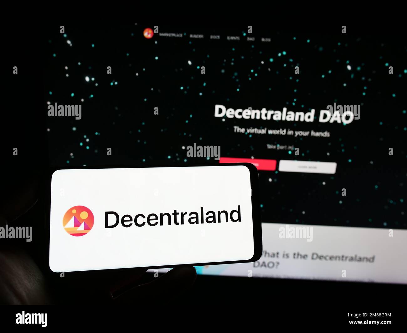 Persona che tiene uno smartphone con il logo della piattaforma virtuale Decentraland sullo schermo di fronte al sito Web. Messa a fuoco sul display del telefono. Foto Stock