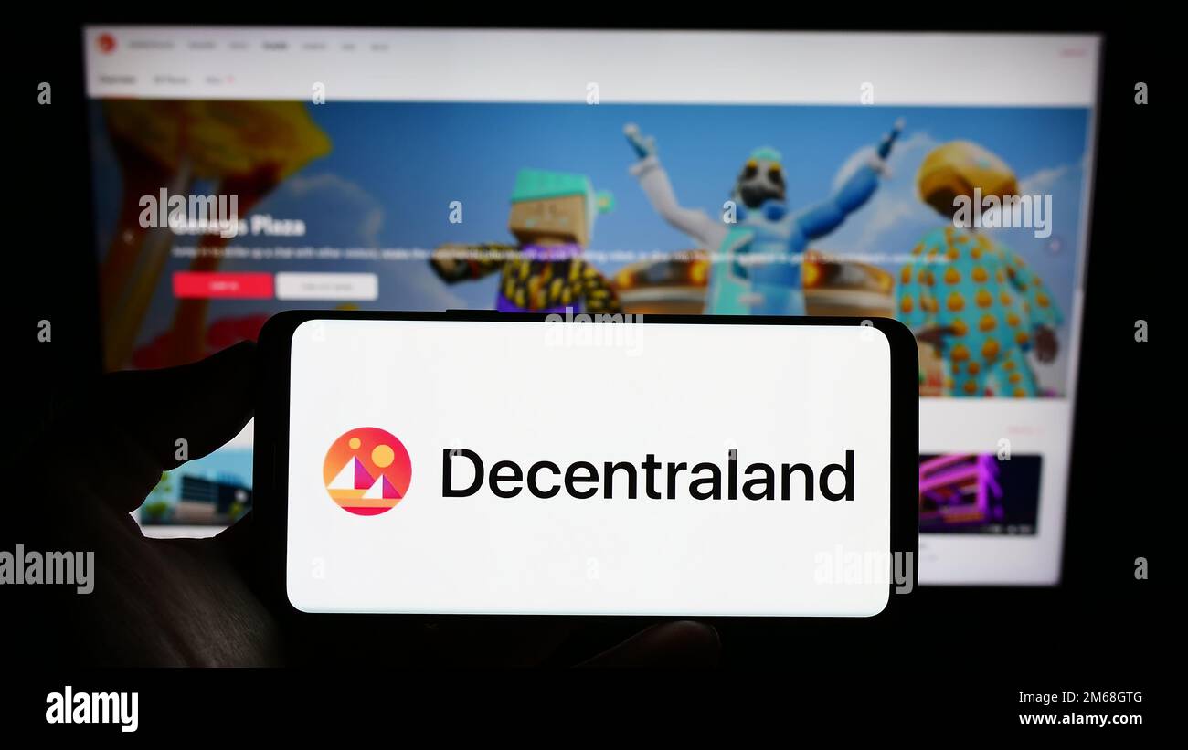 Persona che tiene il cellulare con il logo della piattaforma virtuale del mondo Decentraland sullo schermo di fronte alla pagina web. Messa a fuoco sul display del telefono. Foto Stock