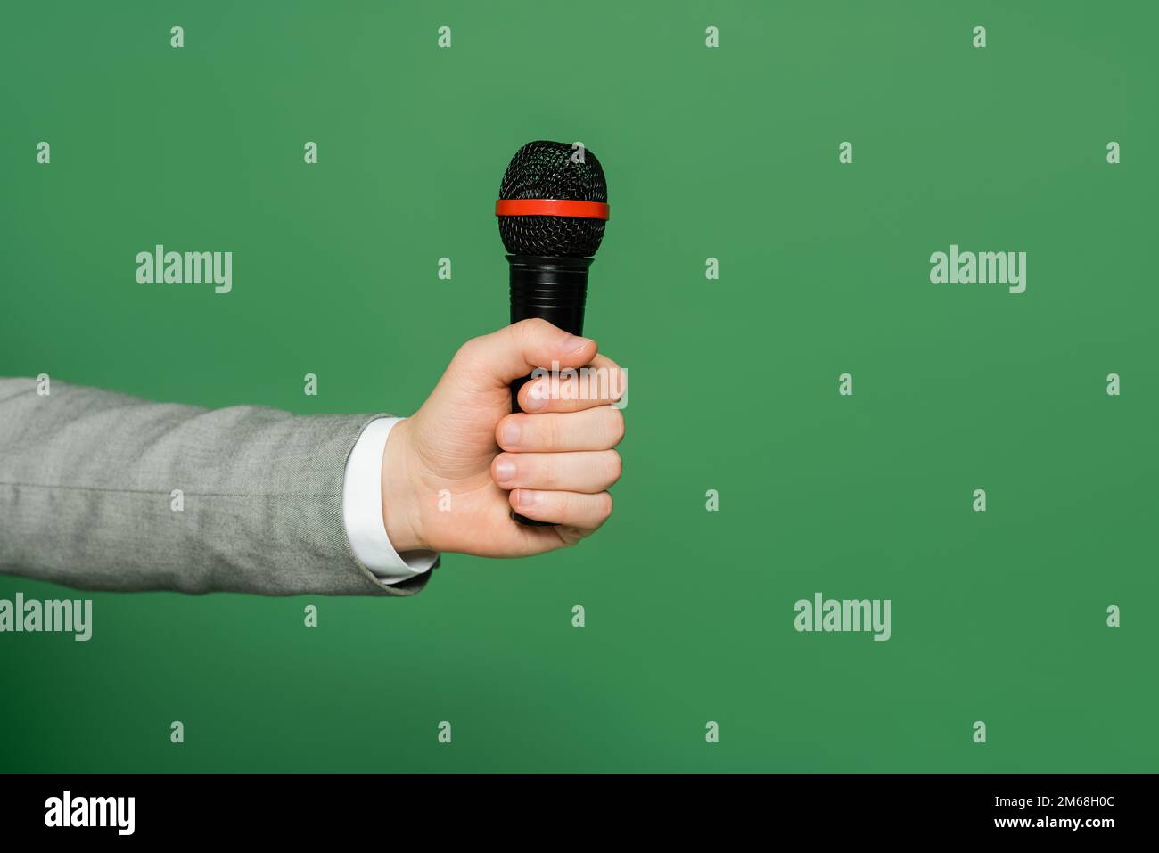 vista ritagliata del giornalista che tiene il microfono in mano isolato sul verde, immagine stock Foto Stock