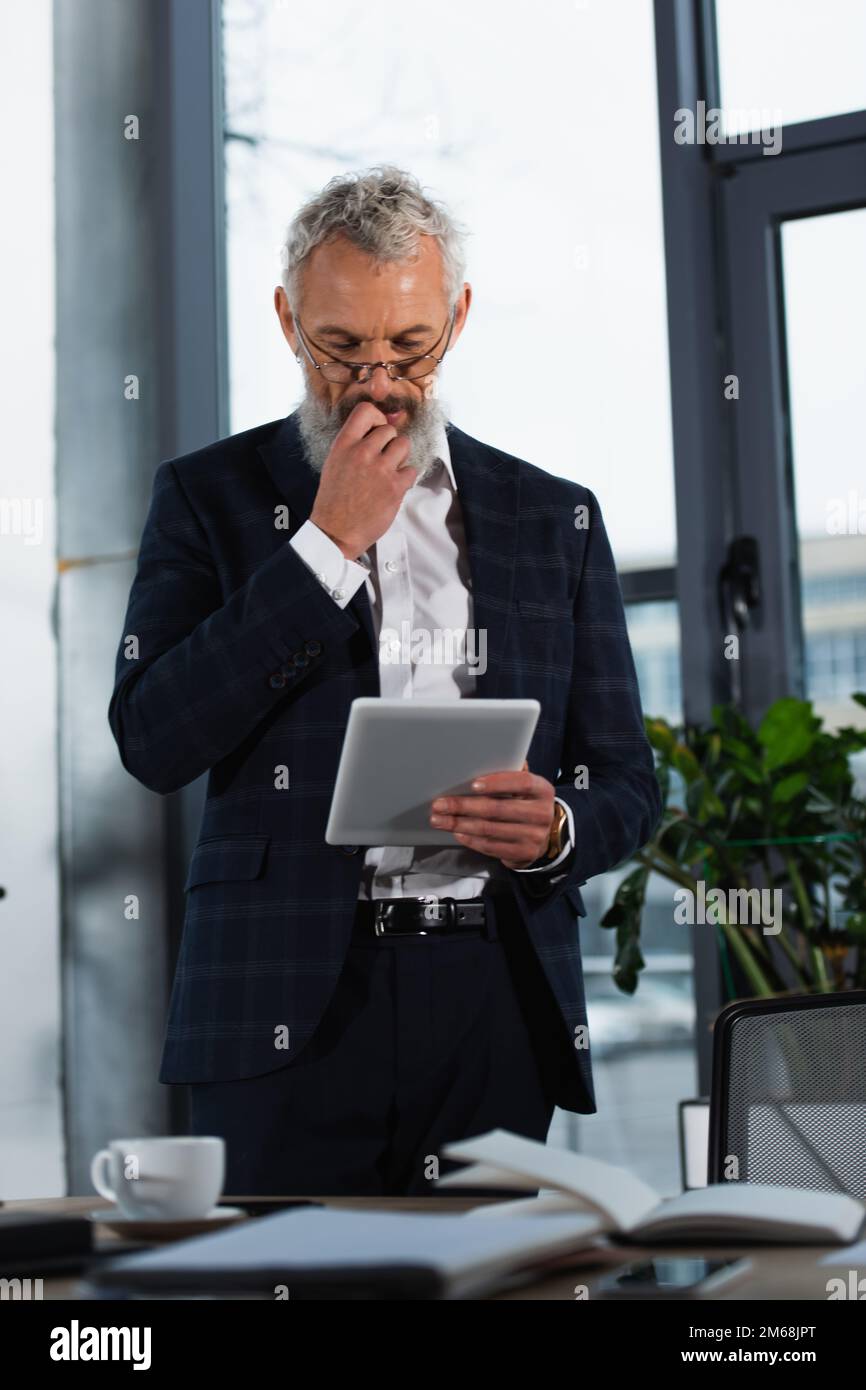 Responsabile concentrato che guarda il tablet digitale in ufficio, immagine stock Foto Stock