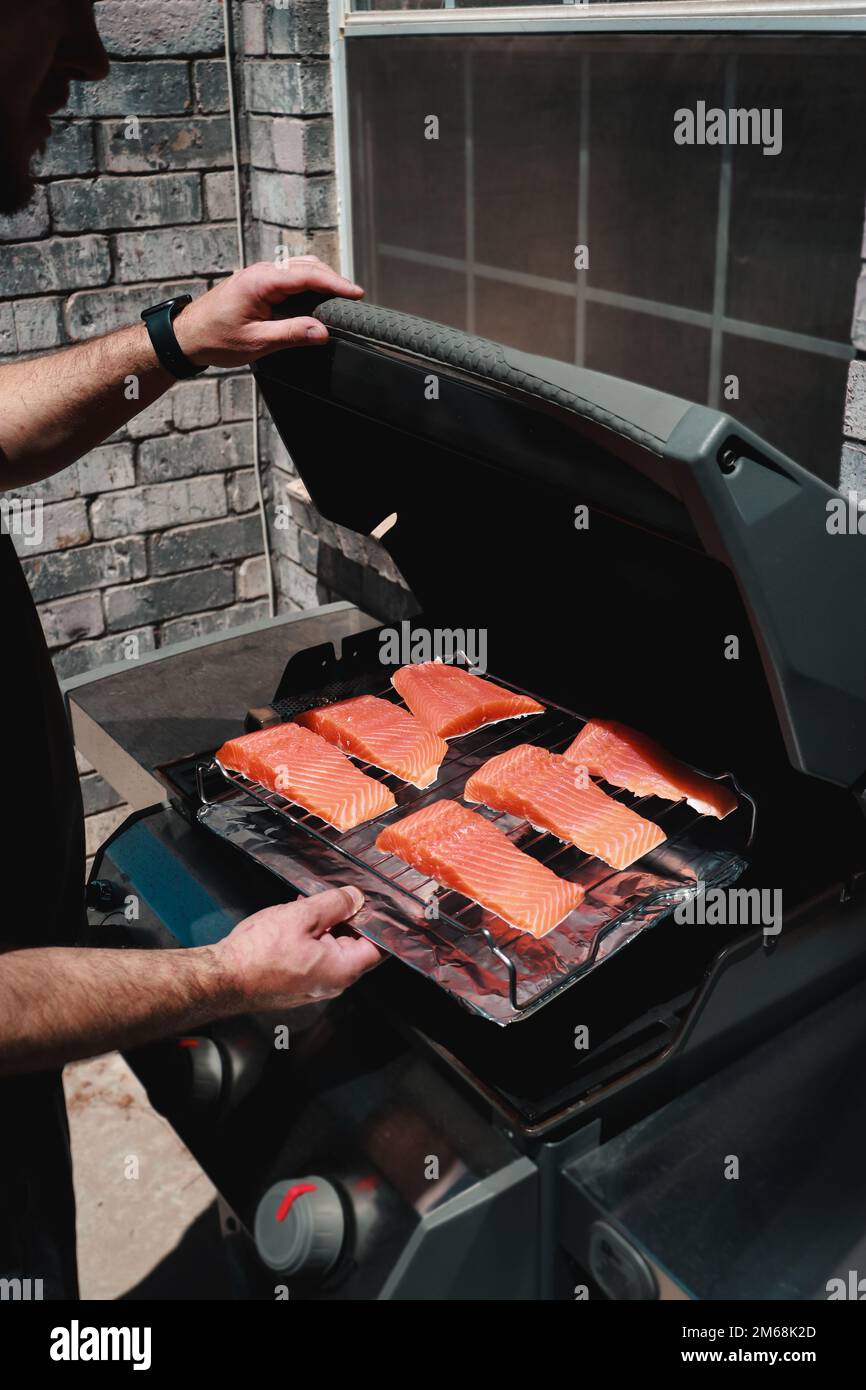 primo piano dell'uomo che mette bistecche di salmone fresco su una griglia Foto Stock