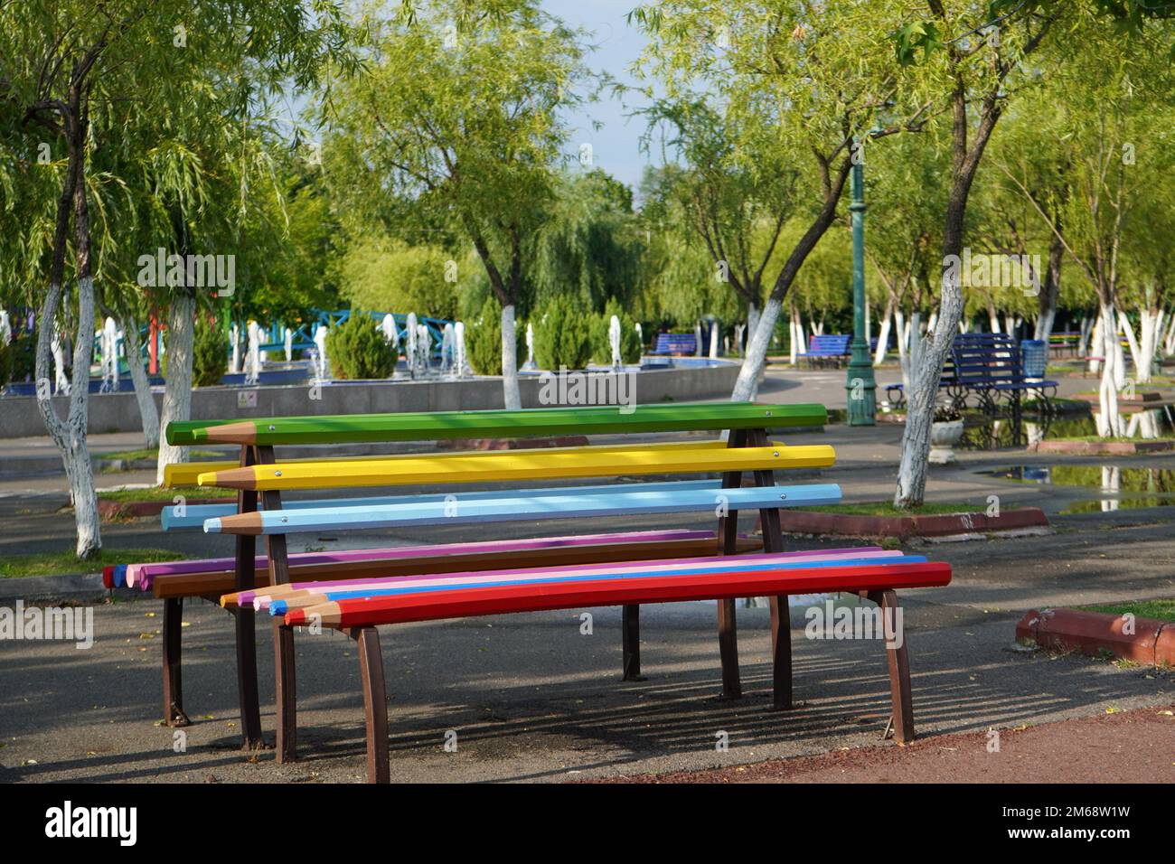 Panca fatta di doghe di legno a forma di pastelli di colori diversi con alberi verdi dietro nel parco di Bucarest Foto Stock