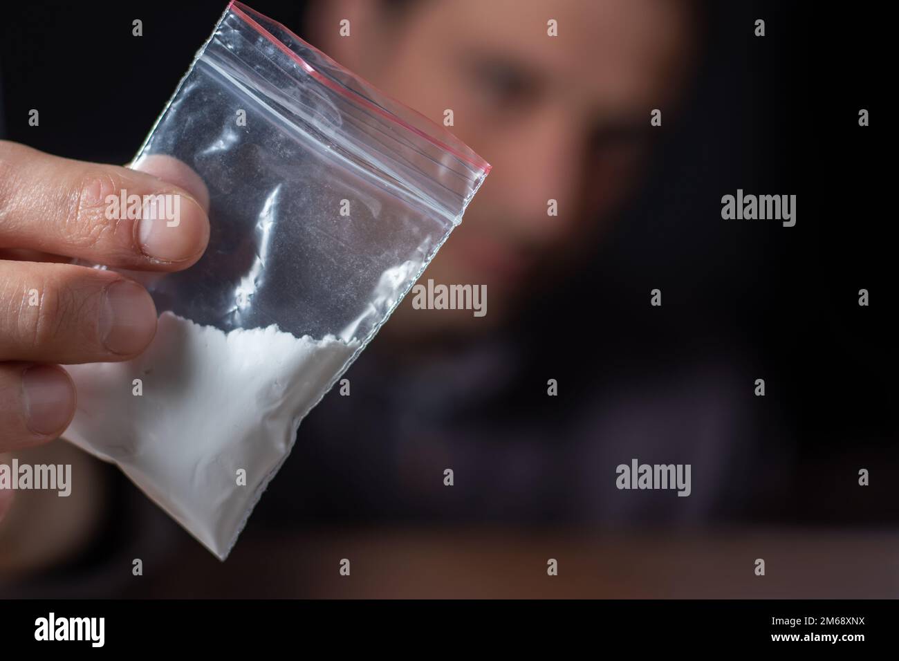 Concetto di tossicodipendenza. La mano dell'uomo tiene il pacchetto o il sacchetto di plastica con la cocaina o altre droghe, l'abuso della droga e il concetto di dipendenza di pericolo. Foto Stock