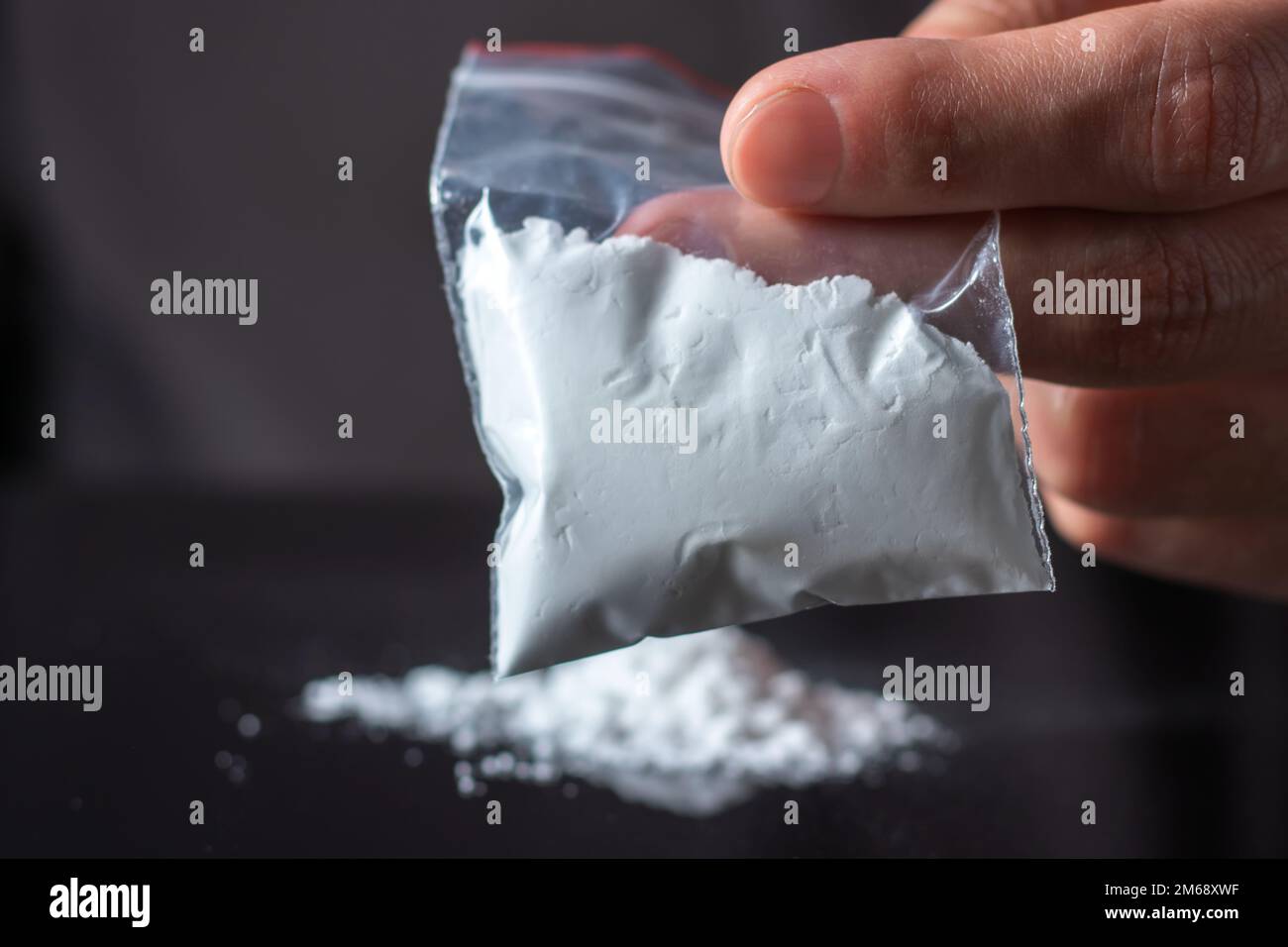 Concetto di tossicodipendenza. La mano dell'uomo tiene il pacchetto o il sacchetto di plastica con la cocaina o altre droghe, l'abuso della droga e il concetto di dipendenza di pericolo. Foto Stock