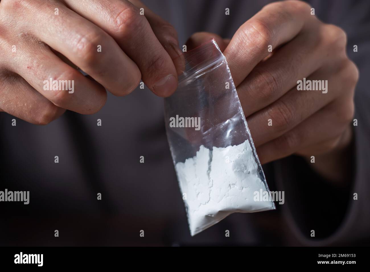 Concetto di tossicodipendenza. La mano dell'uomo tiene il pacchetto o il sacchetto di plastica con la cocaina o altre droghe, l'abuso della droga e il concetto di dipendenza di pericolo. Foto Stock