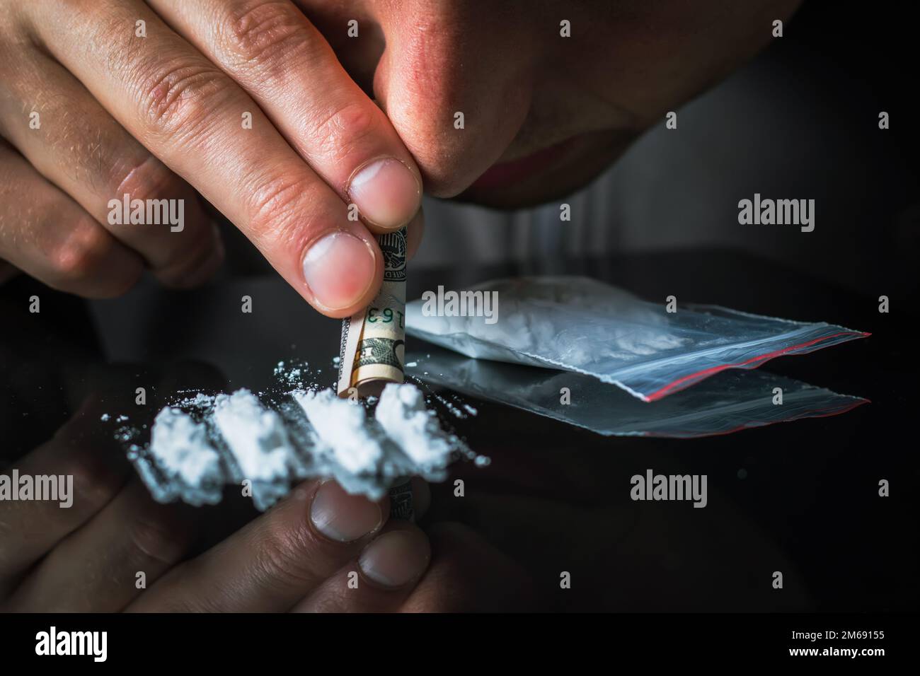 Le mani dell'uomo rotola la banconota per usare le linee della polvere della cocaina. Concetto di tossicodipendenza. Una linea di coke su sfondo nero. Concetto di dipendenza. Mefedrone, Foto Stock