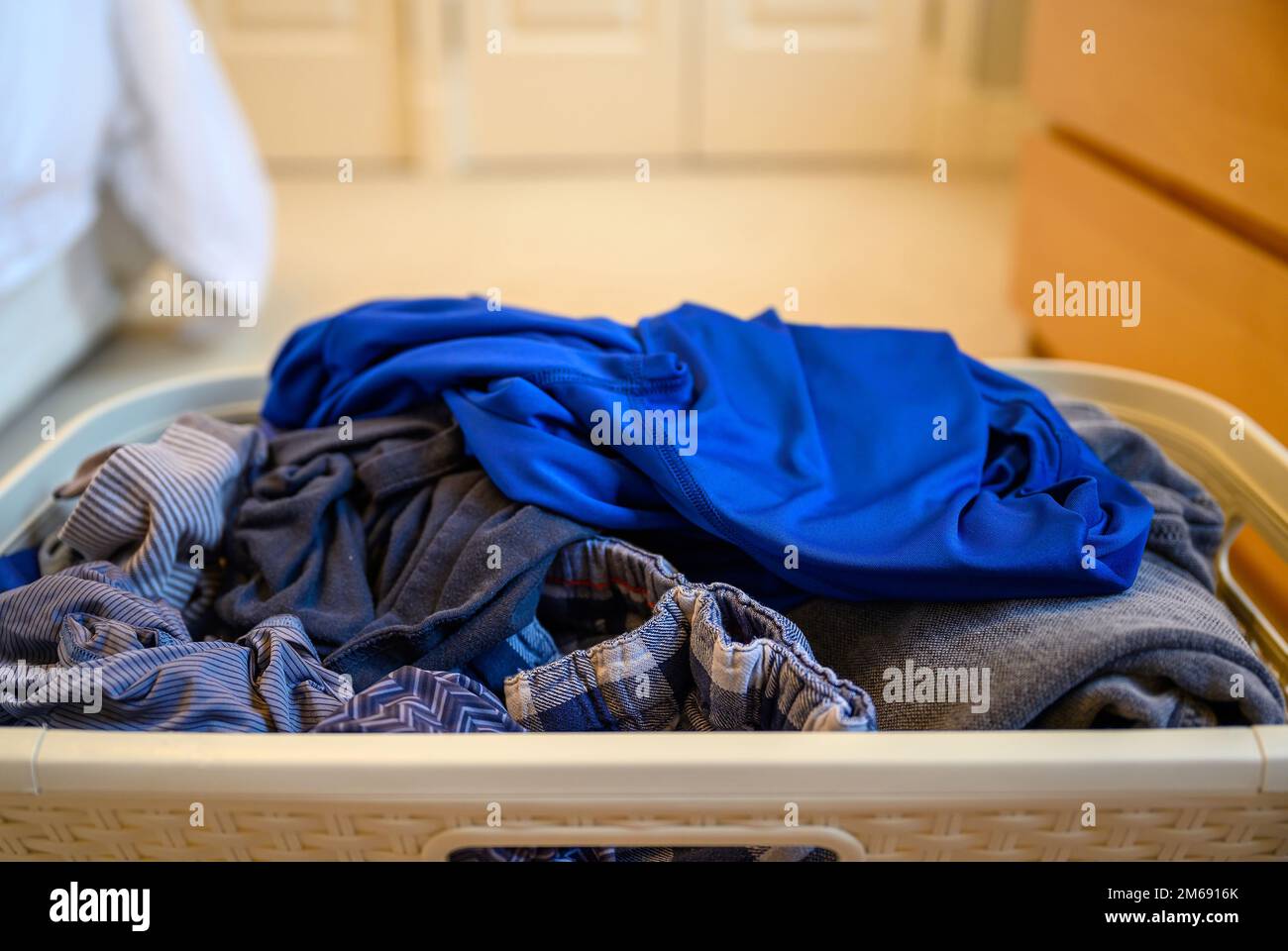 Cestino di bucato pulito in una camera da letto. Disposizione casuale dei vestiti nel cestino che osservano sudicio. Foto Stock