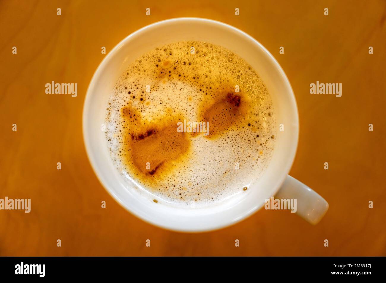 Tazza di caffè su un tavolo visto dall'alto. Caffè latte macchiato con macchie di caffè sulla parte superiore della bevanda e bolle nella schiuma. Foto Stock