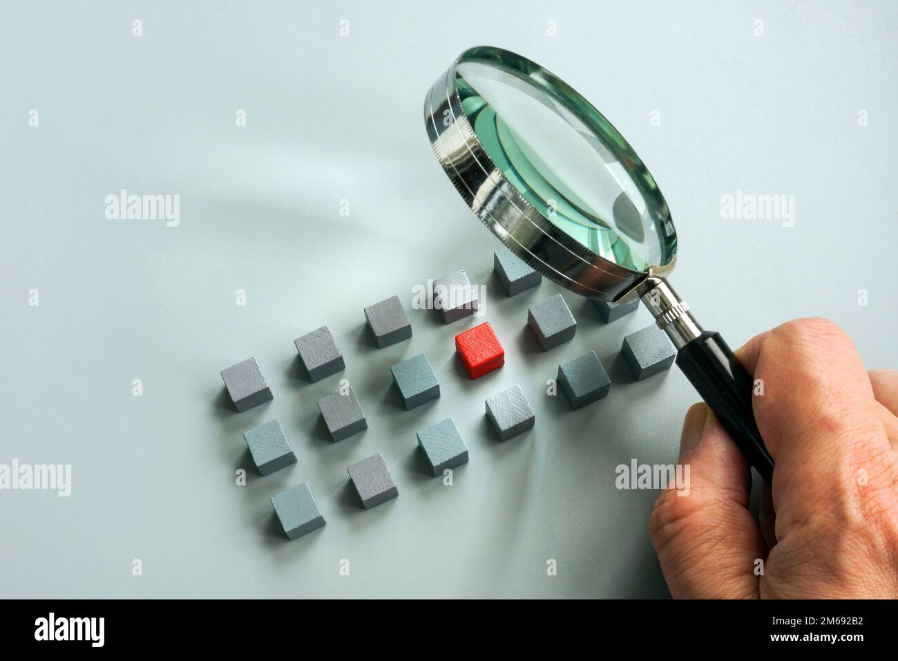 Concetto di gestione dei talenti. Una mano con una lente d'ingrandimento sopra i cubi grigi ed una rossa. Foto Stock