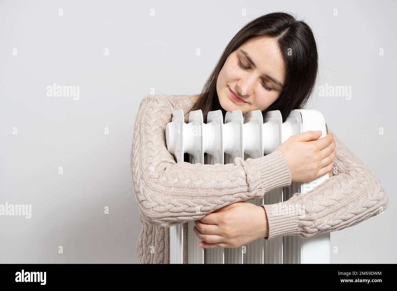 Una donna brunetta abbraccia un riscaldatore elettrico dell'olio, si riscalda in inverno. Foto Stock