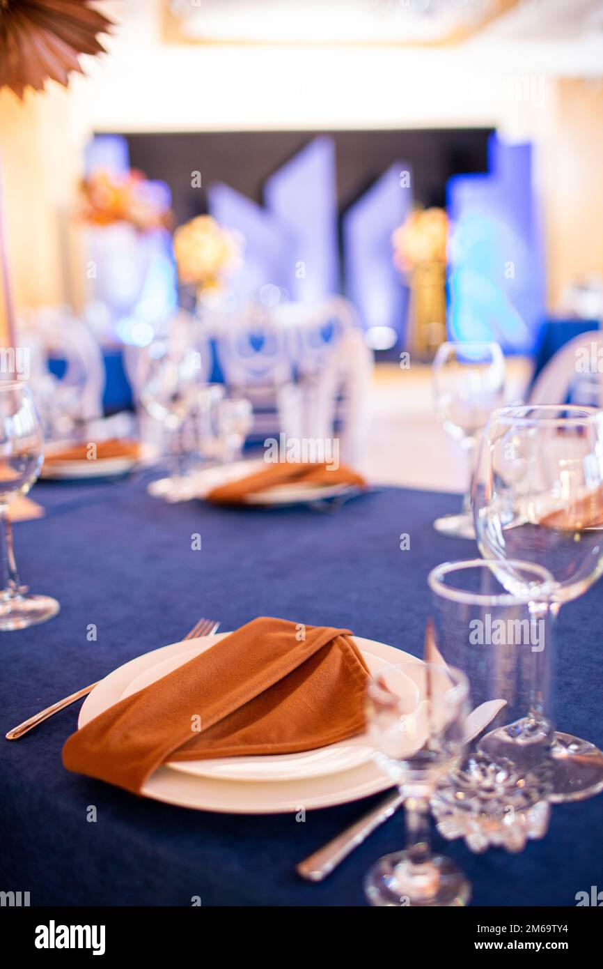 Tavolo festivo con stoffa blu, tovaglioli, piatti, posate e bicchieri  preparati per gli ospiti del matrimonio nel ristorante. Bella composizione  floreale in oro me Foto stock - Alamy