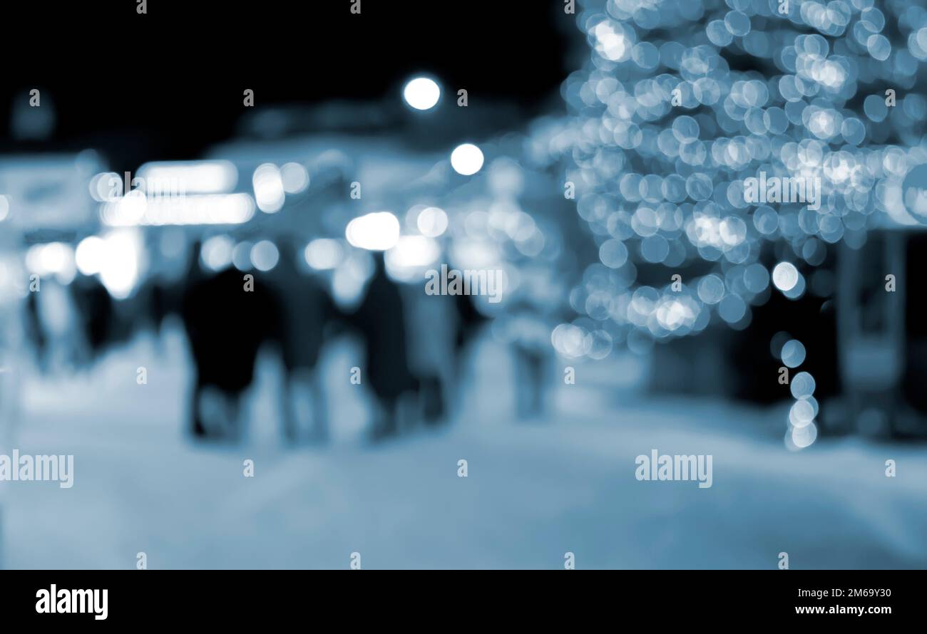 Sfondo sfocato. Albero di Natale, luci luminose decorate, silhouette di costruzione di persone che camminano la piazza della città durante la notte d'inverno. Bello Capodanno e Natale vacanza sfondo sfocato colore blu Foto Stock