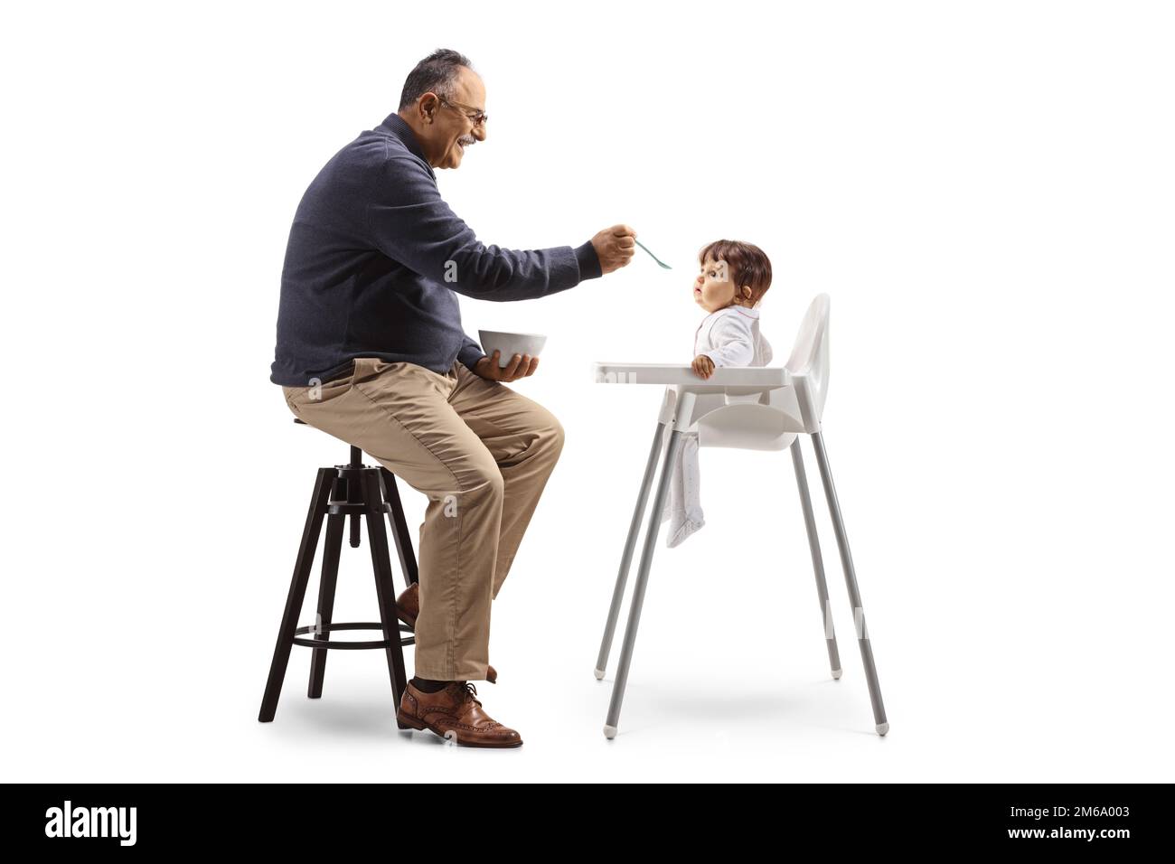 Inquadratura di un uomo maturo seduto e che allatta un bambino con un cucchiaio isolato su sfondo bianco Foto Stock