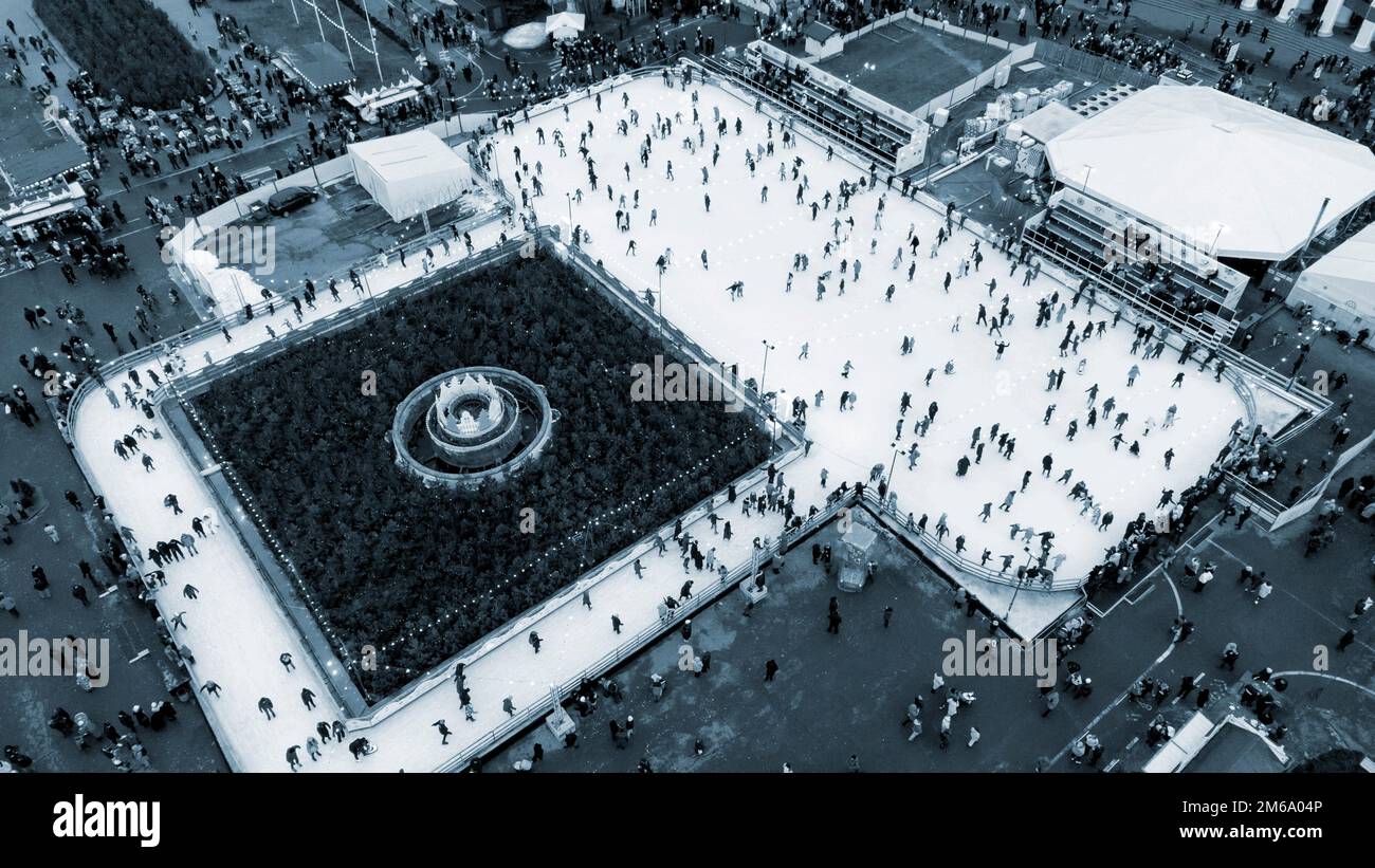 Molte persone pattinano sulla pista di pattinaggio su ghiaccio bianco all'aperto il giorno d'inverno. Vista aerea del drone. Capodanno Natale celebrazione sfondo vacanze. Paesaggio urbano. Divertimento attivo Lifestyle ricreazione colore blu Foto Stock