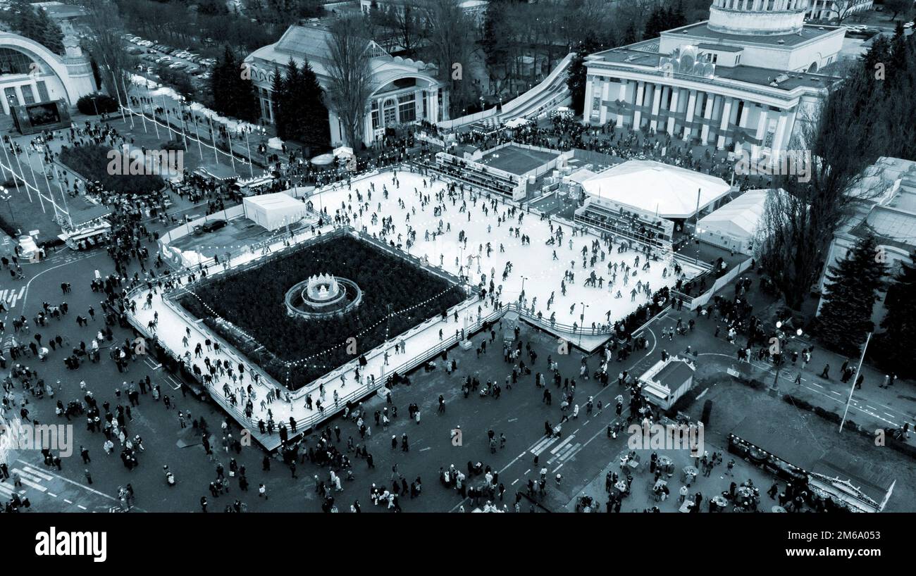 Vista panoramica aerea del parco urbano, pista di pattinaggio su ghiaccio all'aperto e molte persone. Persone che pattinano sulla pista di pattinaggio su ghiaccio. Parco pubblico. Capodanno Natale celebrazione sfondo vacanze. Colore blu Foto Stock