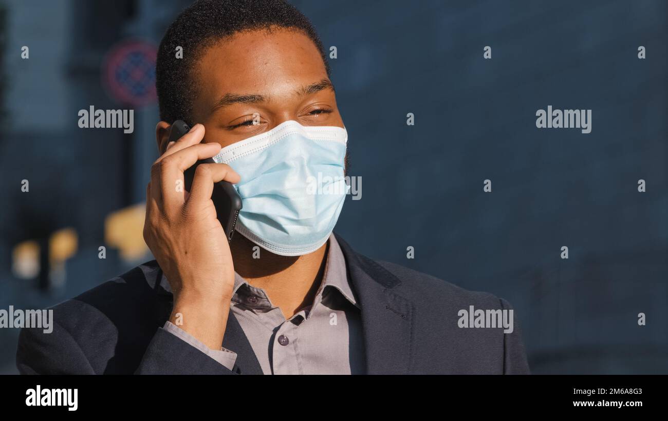Uomo d'affari afro-americano uomo etnico uomo maschio ragazzo in maschera medica parlare telefono cellulare rispondere chiamata parlare con smartphone chiamata parlare con Foto Stock