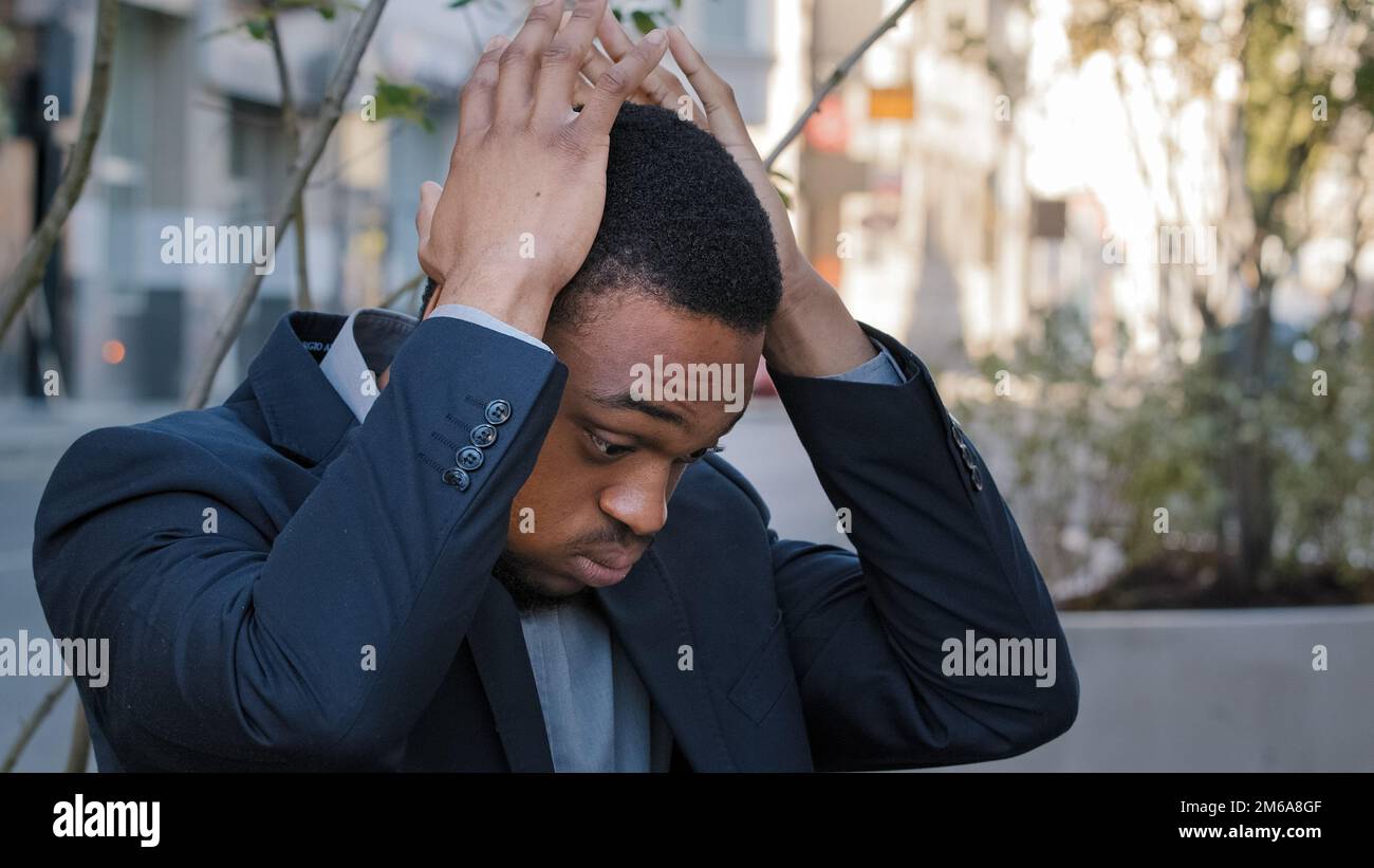 Stressato uomo etnico esausto ragazzo maschio azienda dipendente che ha dolore alla testa mal di testa stress mal di testa con perdita di lavoro licenziato disoccupazione in città. Stanco Foto Stock