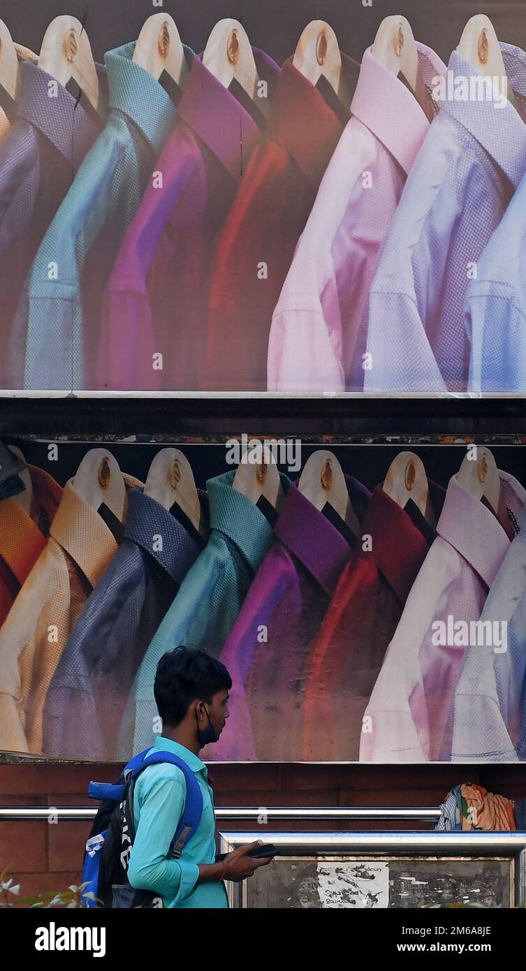 Un uomo in possesso di un telefono cellulare passa davanti alla pubblicità della camicia degli uomini in un rifugio per autobus. Le vendite delle aziende di abbigliamento e dei marchi lifestyle a livello globale sono salite tra il 30% e il 70% nell'anno finanziario (FY) 2022, modificando il margine di profitto rispetto a un anno in cui il 19 ha dovuto affrontare restrizioni indotte che hanno causato una contrazione delle attività e delle vendite aziendali. Foto Stock