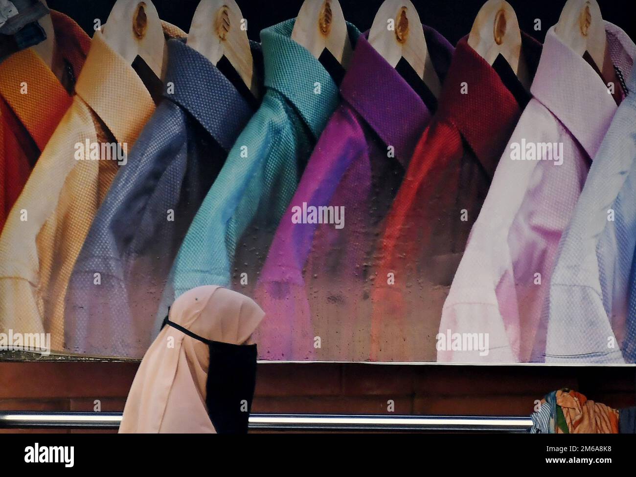 Una donna musulmana passa davanti alla pubblicità della camicia maschile in un rifugio di autobus. Le vendite delle aziende di abbigliamento e dei marchi lifestyle a livello globale sono salite tra il 30% e il 70% nell'anno finanziario (FY) 2022, modificando il margine di profitto rispetto a un anno in cui il 19 ha dovuto affrontare restrizioni indotte che hanno causato una contrazione delle attività e delle vendite aziendali. Foto Stock