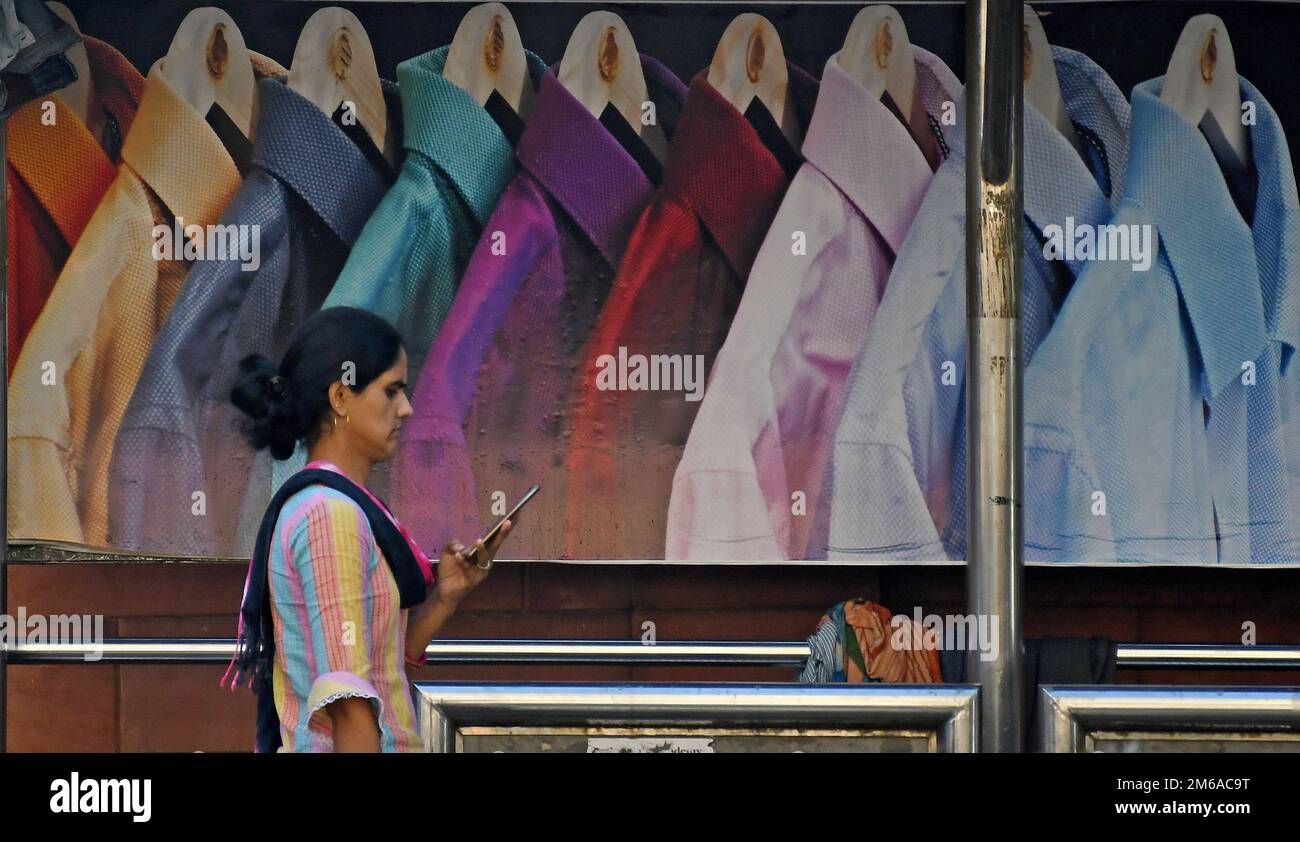 Mumbai, Maharashtra, India. 3rd Jan, 2023. Una donna che tiene un telefono cellulare cammina oltre la pubblicità della camicia degli uomini in un rifugio di autobus. Le vendite delle aziende di abbigliamento e dei marchi lifestyle a livello globale sono salite tra il 30% e il 70% nell'anno finanziario (FY) 2022, modificando il margine di profitto rispetto a un anno in cui il 19 ha dovuto affrontare restrizioni indotte che hanno causato una contrazione delle attività e delle vendite aziendali. (Credit Image: © Ashish Vaishnav/SOPA Images via ZUMA Press Wire) Foto Stock