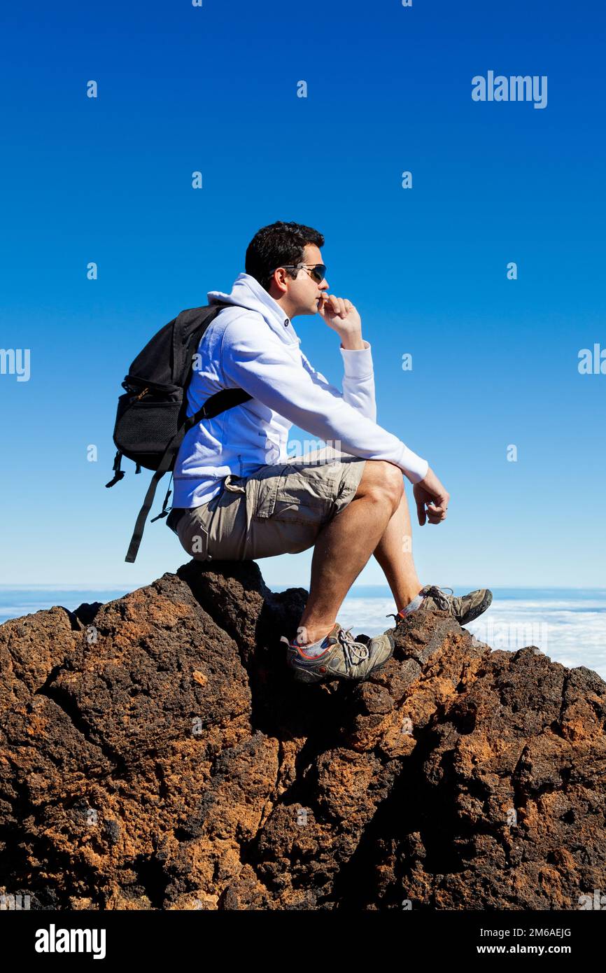 Giovane uomo che riposa in un picco alto sopra le nuvole in montagna di Teide Foto Stock