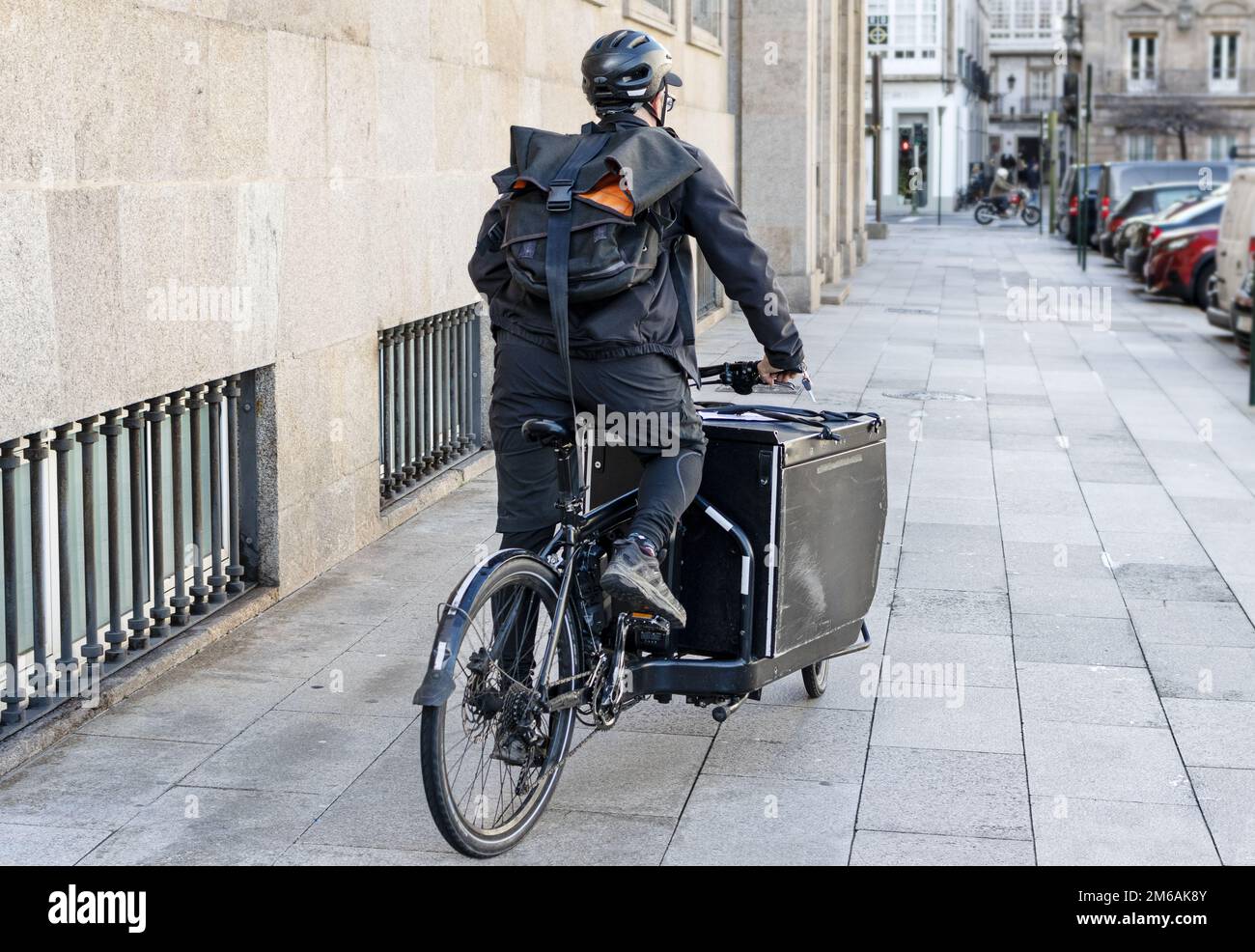 Vista posteriore di Courier uomo a bordo di una bicicletta da carico lungo la città sulla sua strada per consegnare un pacchetto Foto Stock