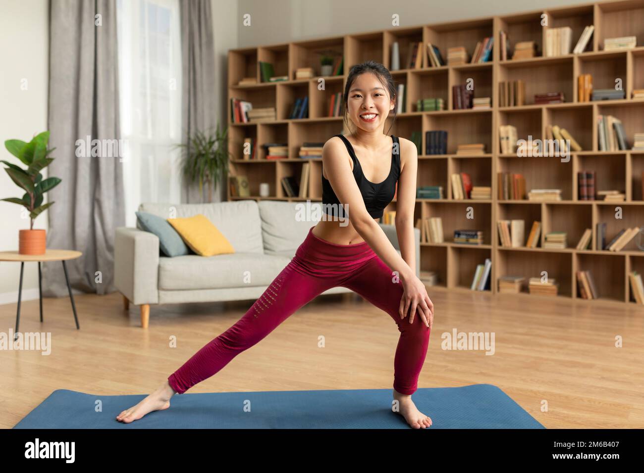 Tutta la lunghezza della donna asiatica felice che fa affondi, esercitandosi nel paese sul tappeto di sport, esercitandosi verso l'esterno la sua resistenza, spazio della copia Foto Stock