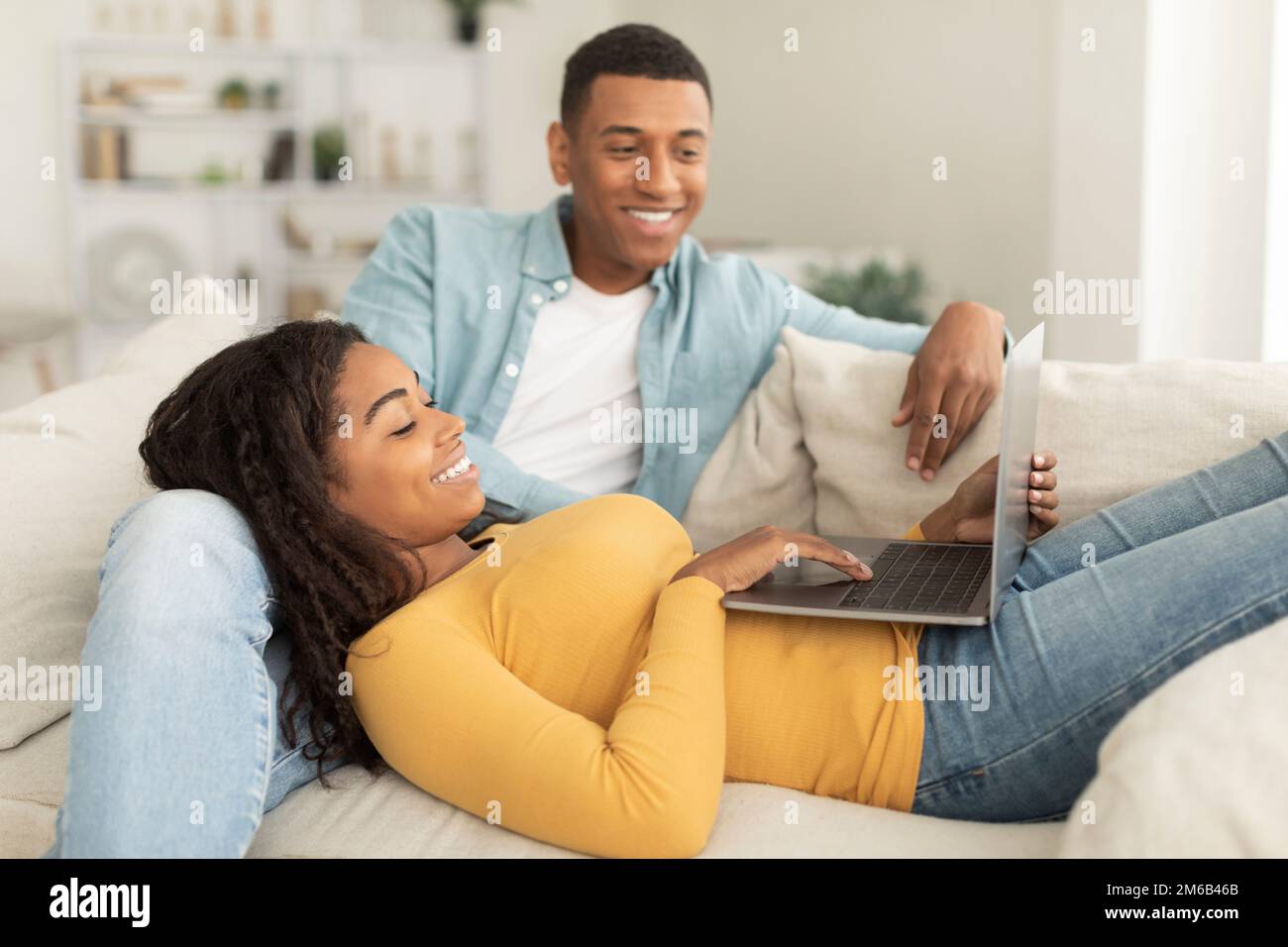 Sorridente uomo e donna afroamericana millenaria, goditi il tempo libero, rilassati sul divano e chiama online Foto Stock