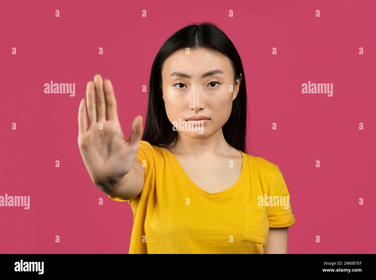 Giovane signora giapponese gesturing STOP, mostrando il gesto di rifiuto, esprimendo il suo atteggiamento negativo, sfondo rosa Foto Stock