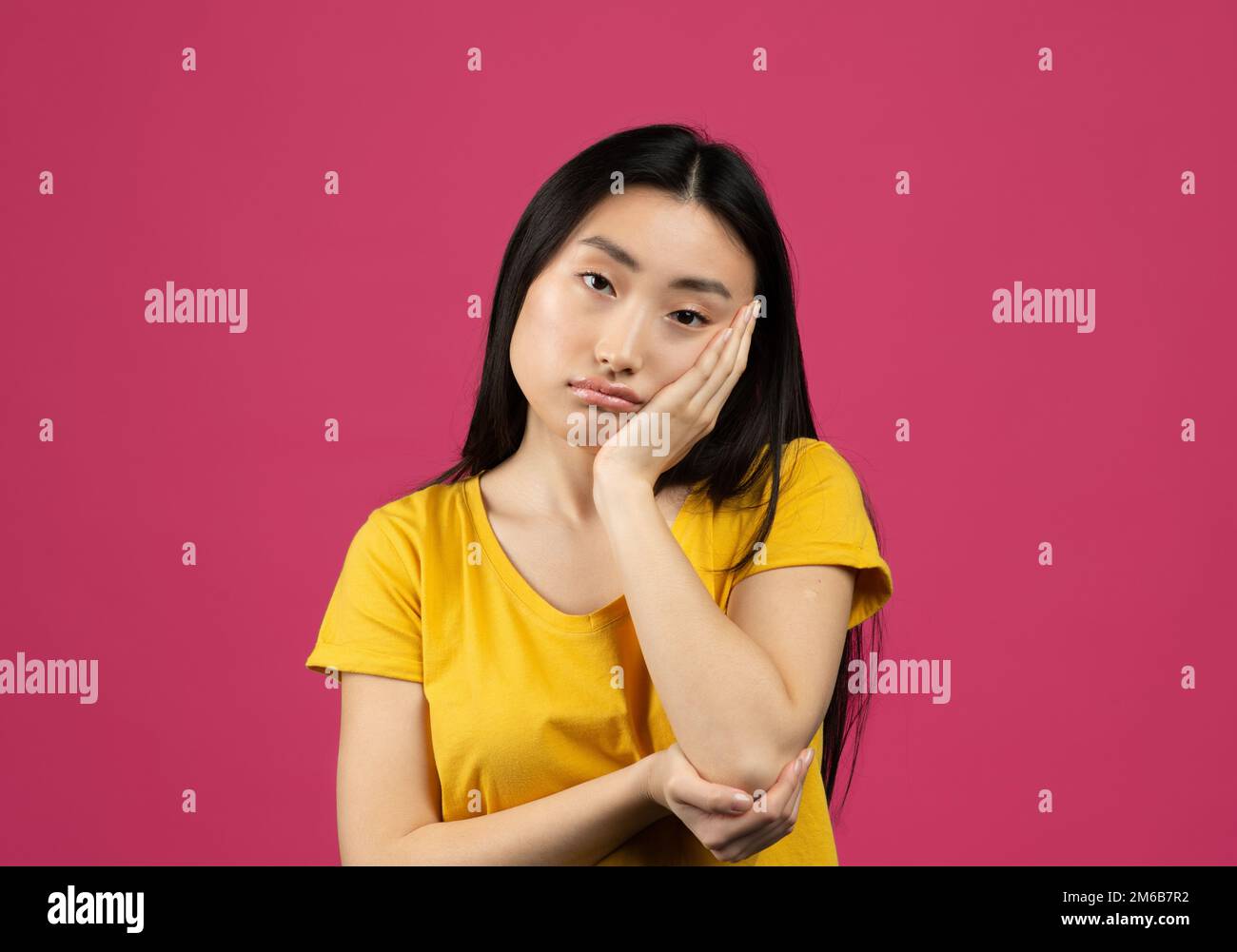 Annoiato giovane donna cinese sentirsi turbata e depressa, guardando la macchina fotografica, posando su sfondo rosa Foto Stock