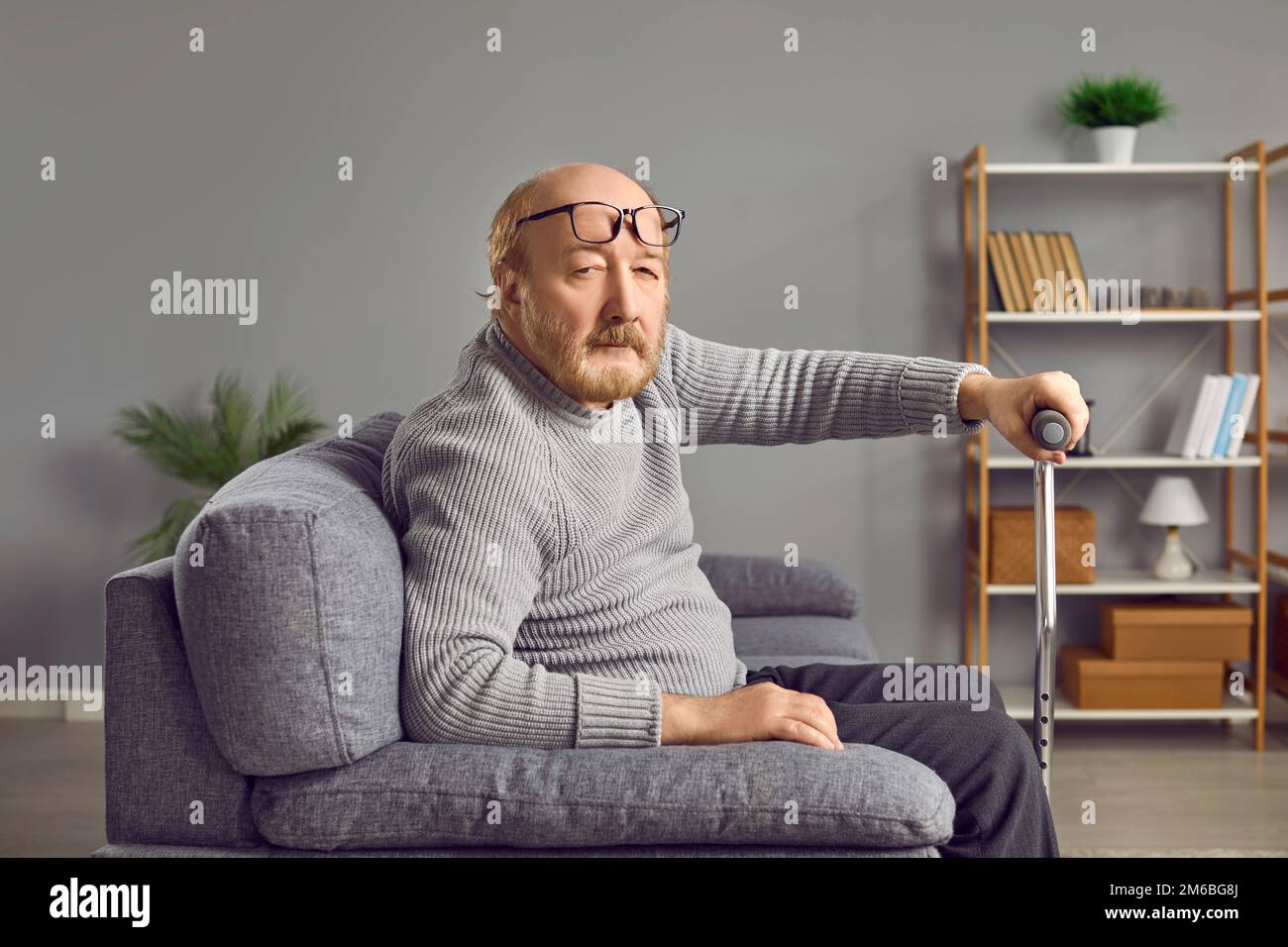 Uomo anziano che tiene il bastone mentre si siede sul divano Foto Stock