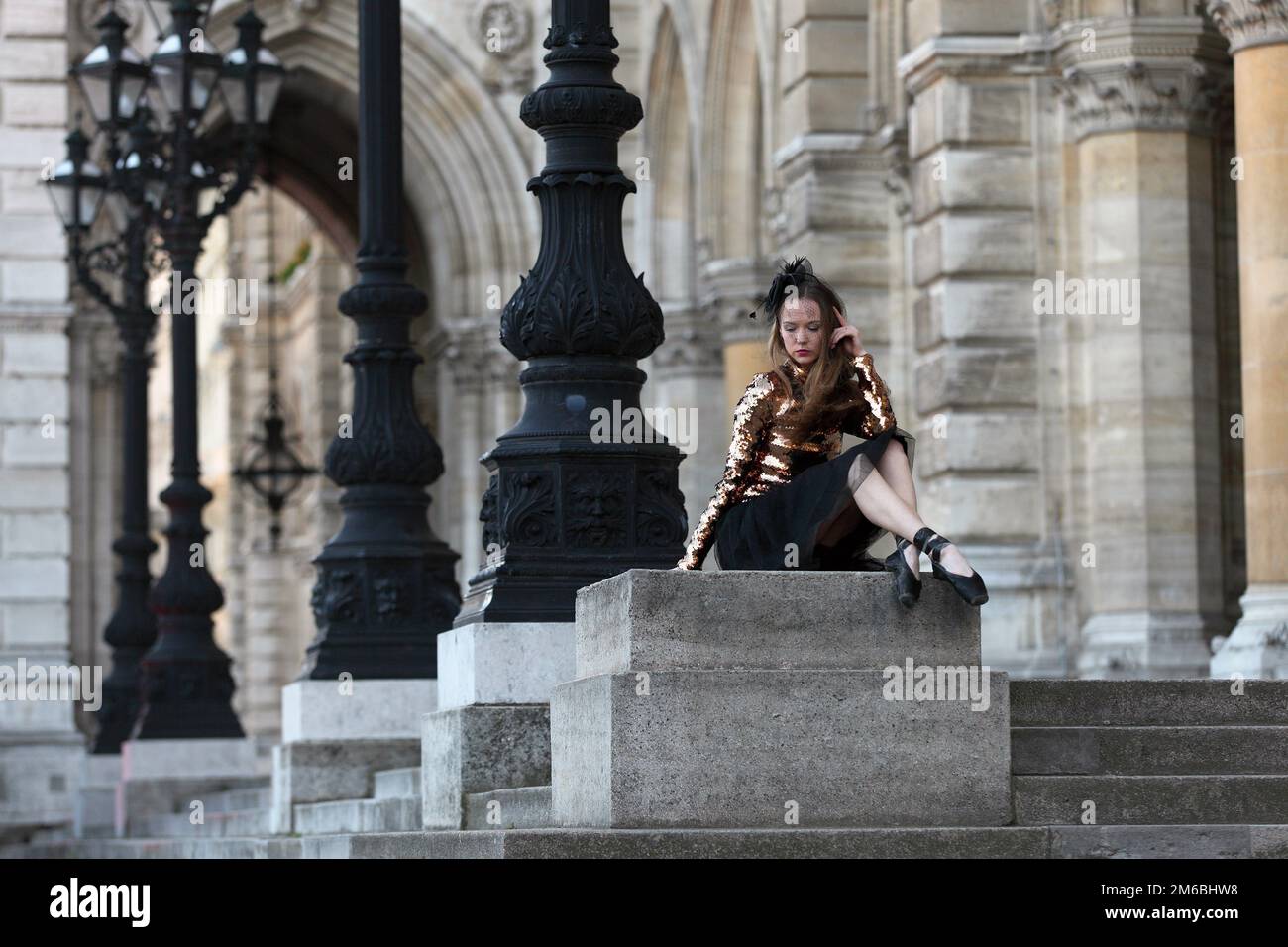 Triste ballerina in gonna nera, foschia e cima dorata seduta di fronte a un palazzo Foto Stock