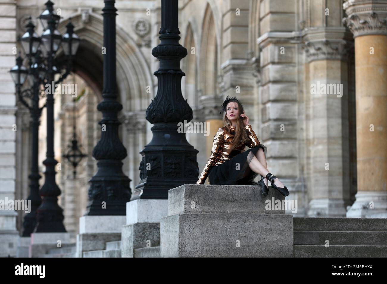 Ballerina melanconca in gonna nera, foschia e cima dorata seduta di fronte a un palazzo Foto Stock