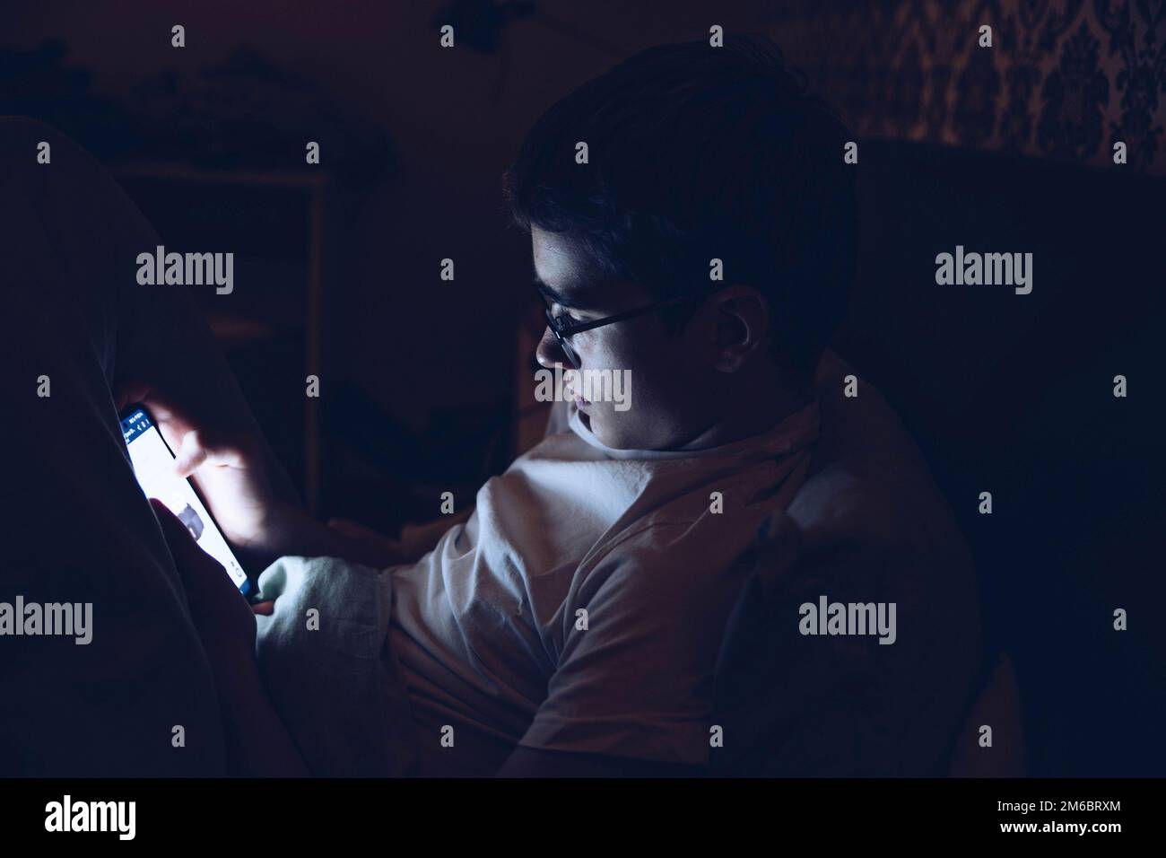 L'adolescente con gli occhiali usa il telefono a letto di notte. Foto Stock