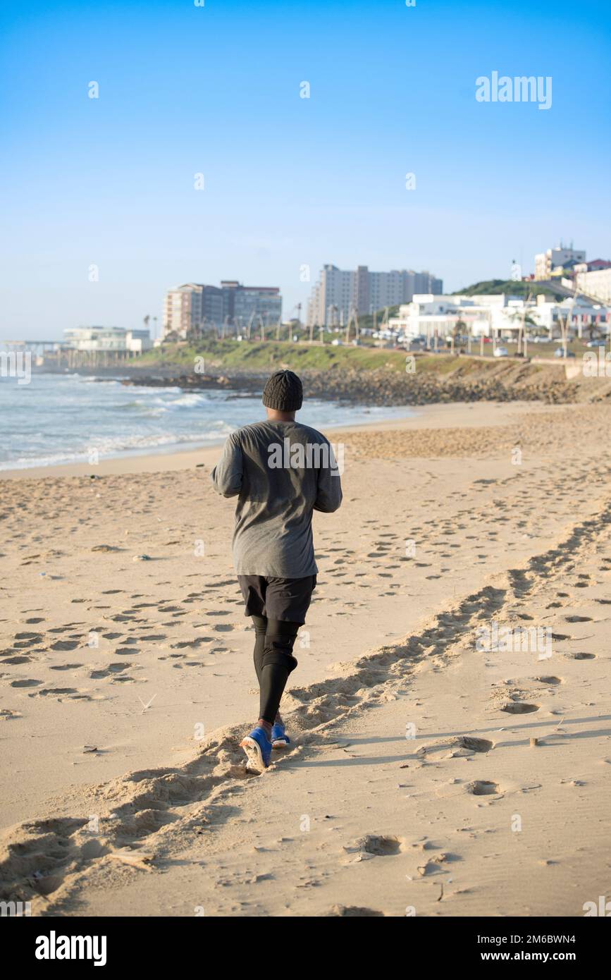 Uomo che fa jogging sulla spiaggia di fronte al paesaggio della città Foto Stock