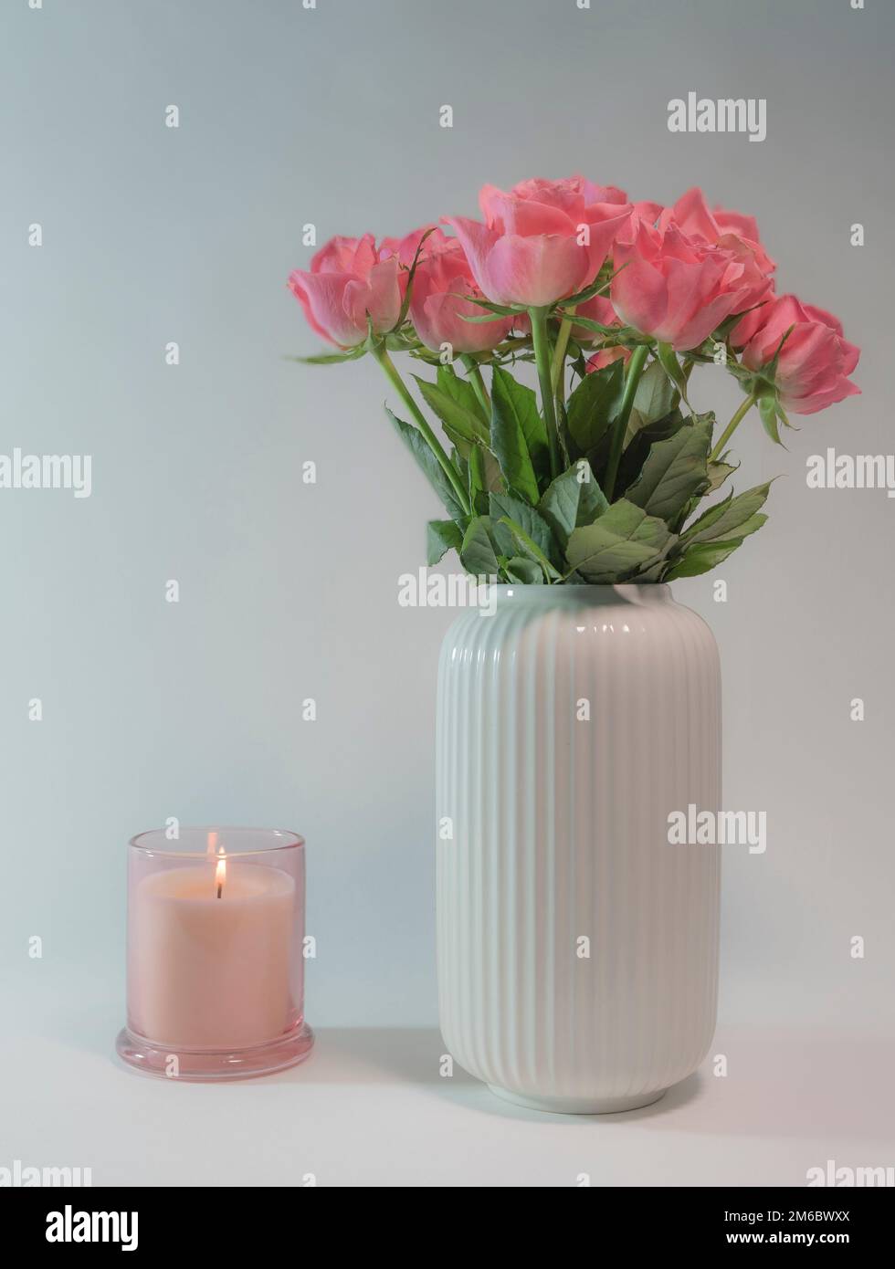 Rosa rose in un vaso e una candela che brucia primo piano Foto Stock