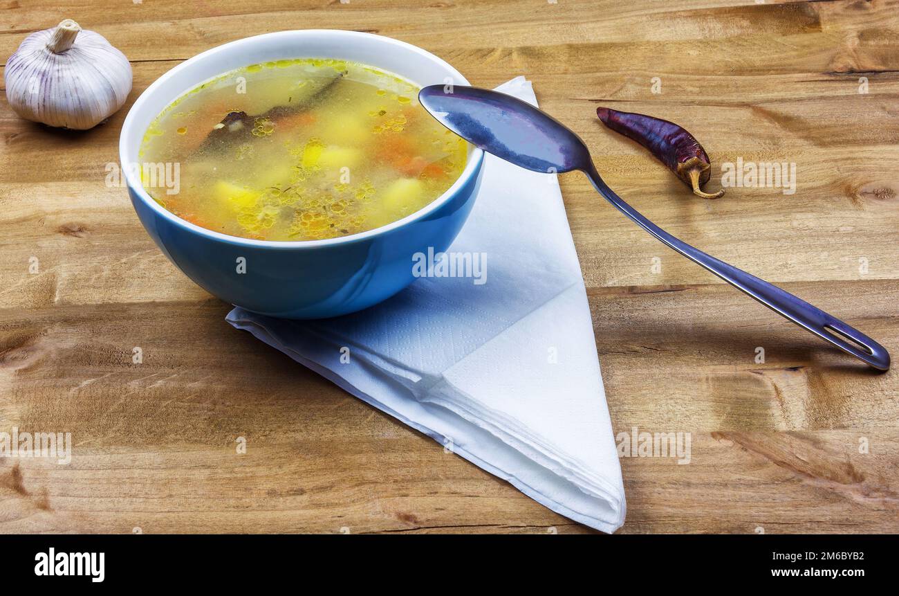 Su un tavolo di legno si trova una ciotola di zuppa e un cucchiaio di metallo Foto Stock