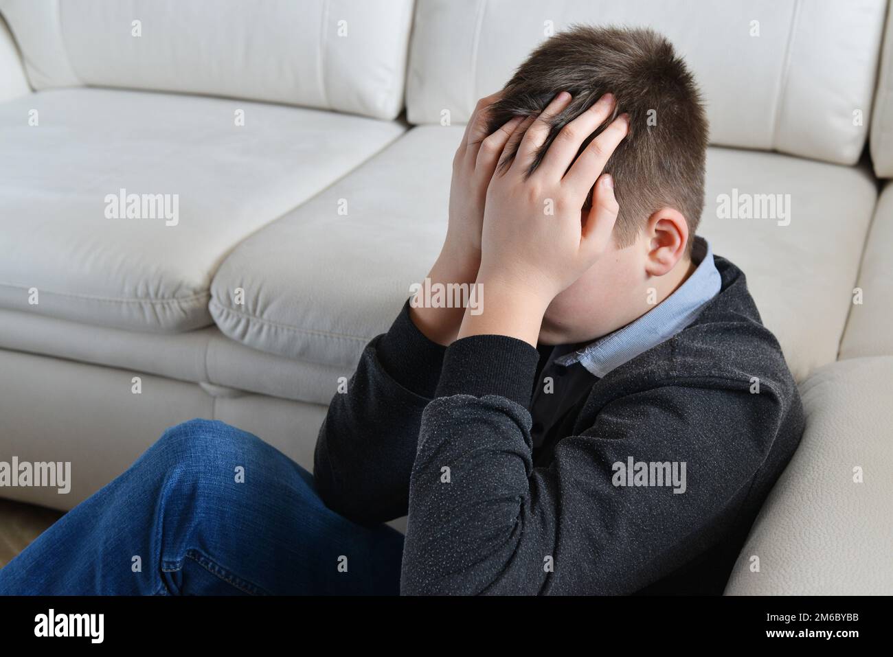 Sconvolto adolescente di 13 anni, si siede vicino al divano che copre il volto con le mani Foto Stock