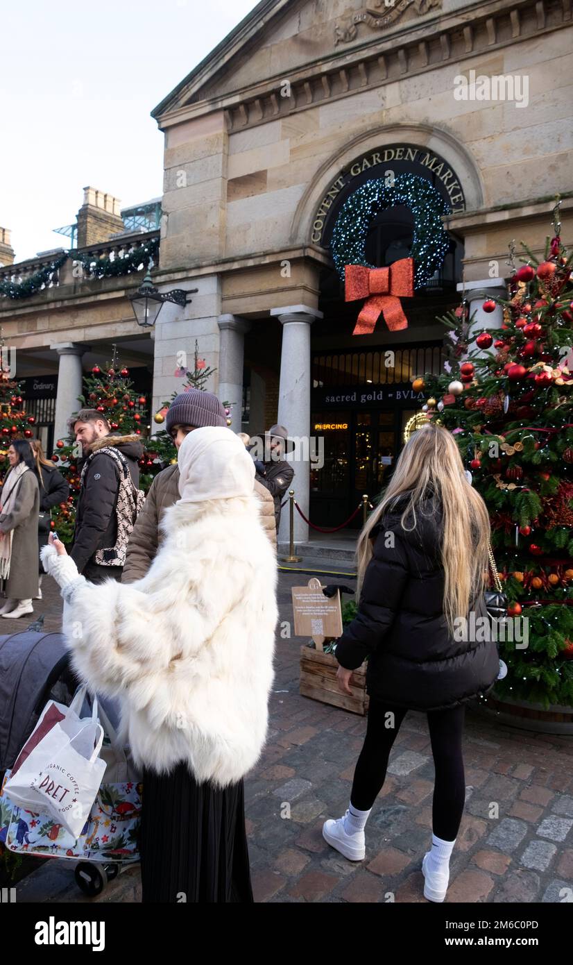 Giovane donna musulmana con velo che guarda il telefono cellulare indossando una giacca di pelliccia bianca nel mercato di Covent Garden Natale tempo Londra UK 2022 KATHY DEWITT Foto Stock