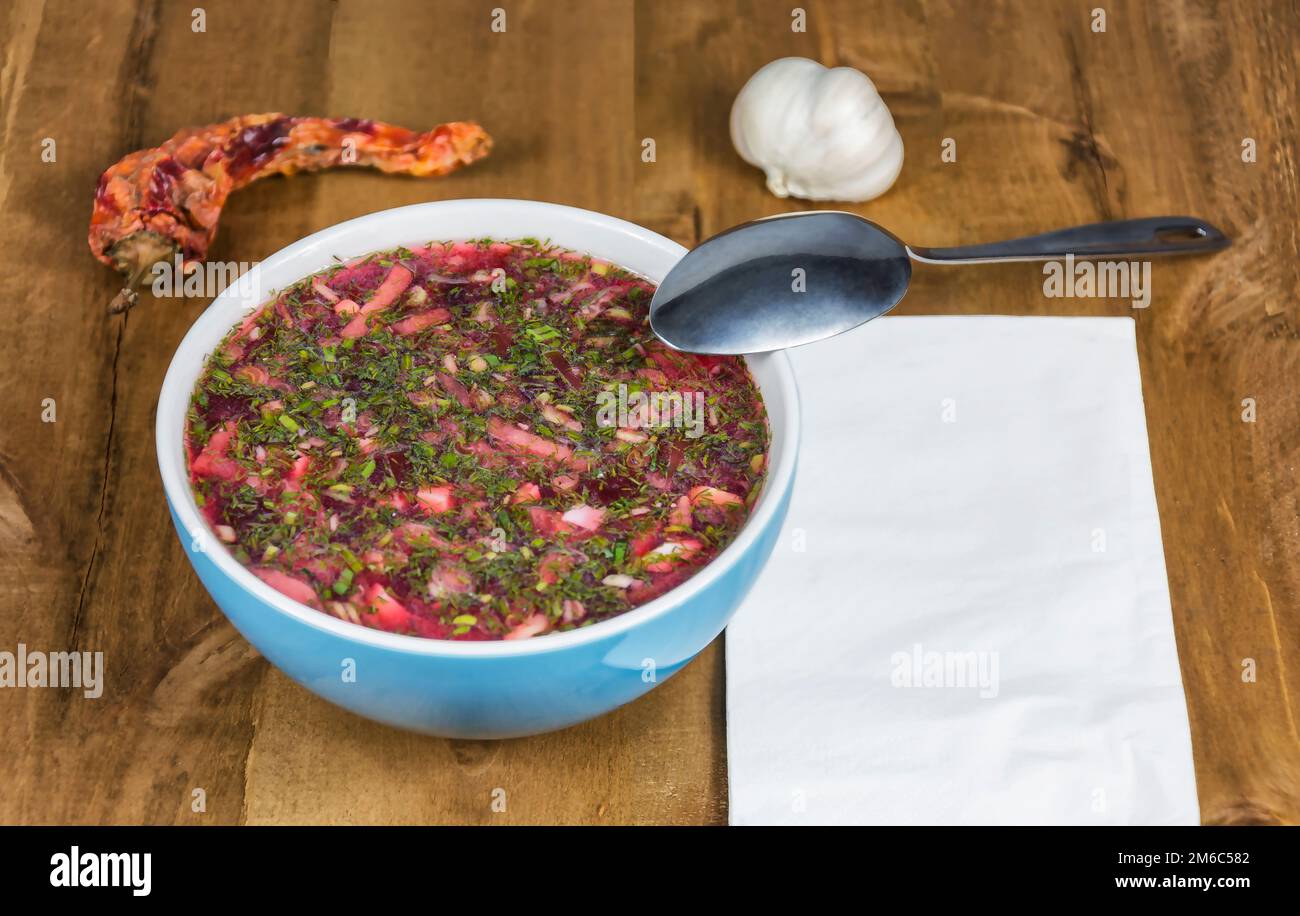 Su un tavolo di legno si trova una ciotola blu di borscht e cucchiaio Foto Stock