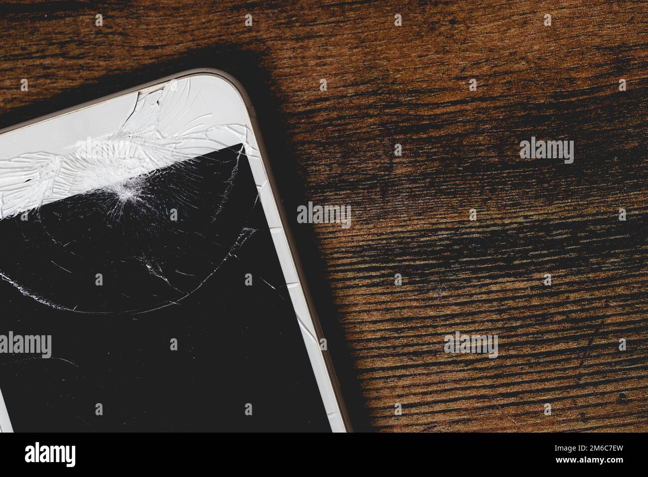 Primo piano di un telefono cellulare danneggiato con schermo incrinato per la riparazione su uno sfondo di legno con spazio copia Foto Stock
