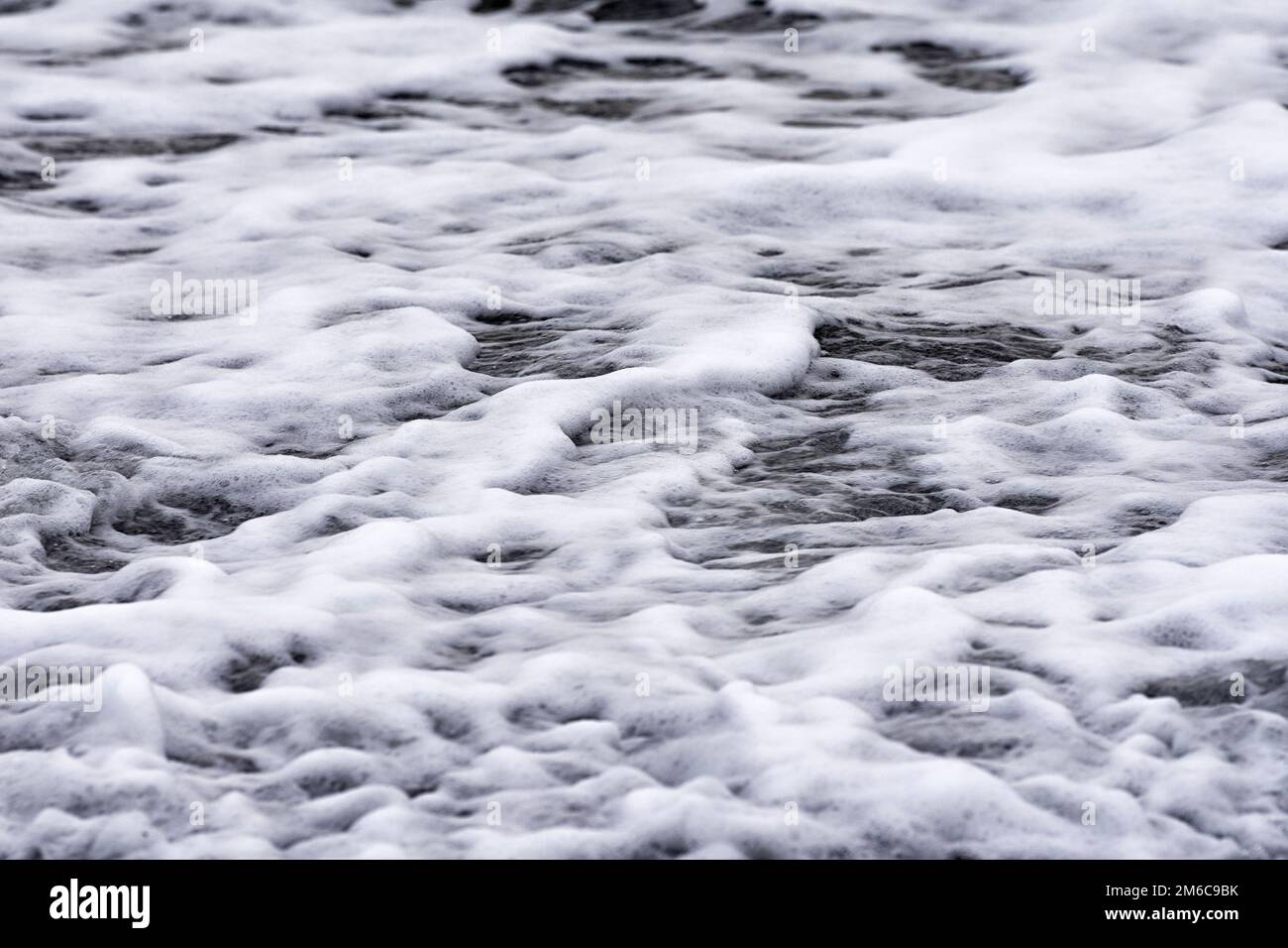 Acqua di mare naturale. L'acqua schiumosa scorre su una spiaggia durante l'inverno. Onde piccole con whitecaps. Mar Baltico, Meclemburgo-Vorpommern, Germania Foto Stock