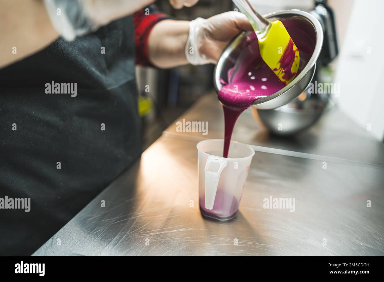Decorazione di pasticceria. Il pasticcere prepara la glassa rosa fusa da una ciotola a una tazza. Cucina professionale. Foto di alta qualità Foto Stock