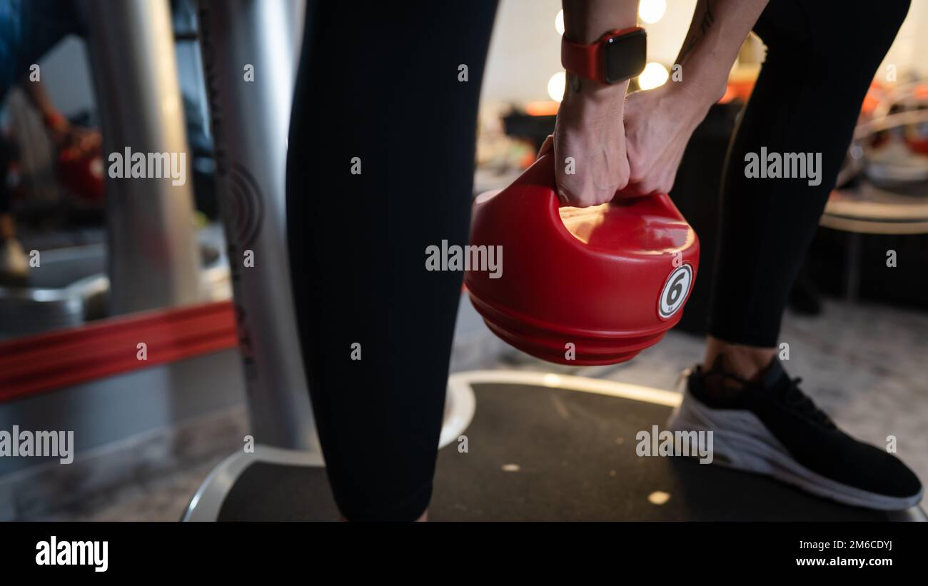Donna sconosciuta tenere rosso Kettlebell peso mentre in piedi sulla piattaforma di vibrazione della piastra di potenza macchina durante l'allenamento squat esercizio copia spazio Foto Stock