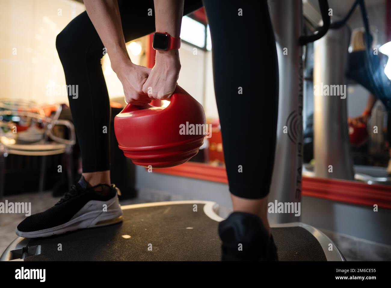 Donna sconosciuta tenere rosso Kettlebell peso mentre in piedi sulla piattaforma di vibrazione della piastra di potenza macchina durante l'allenamento squat esercizio copia spazio Foto Stock