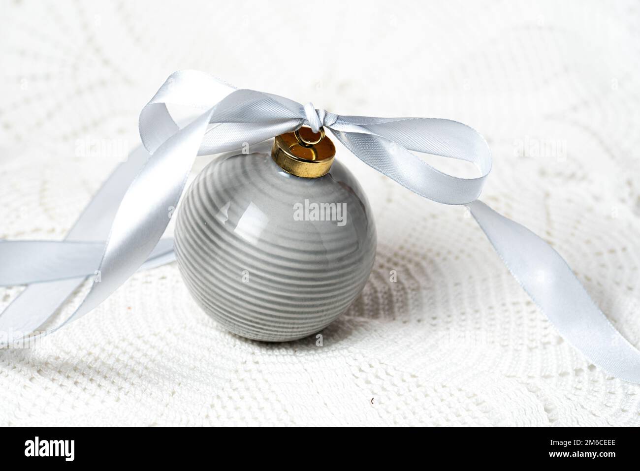 PALLA DI NATALE GRIGIA IN CERAMICA CON NASTRO GRIGIO SU UNA TOVAGLIA IN PIZZO Foto Stock