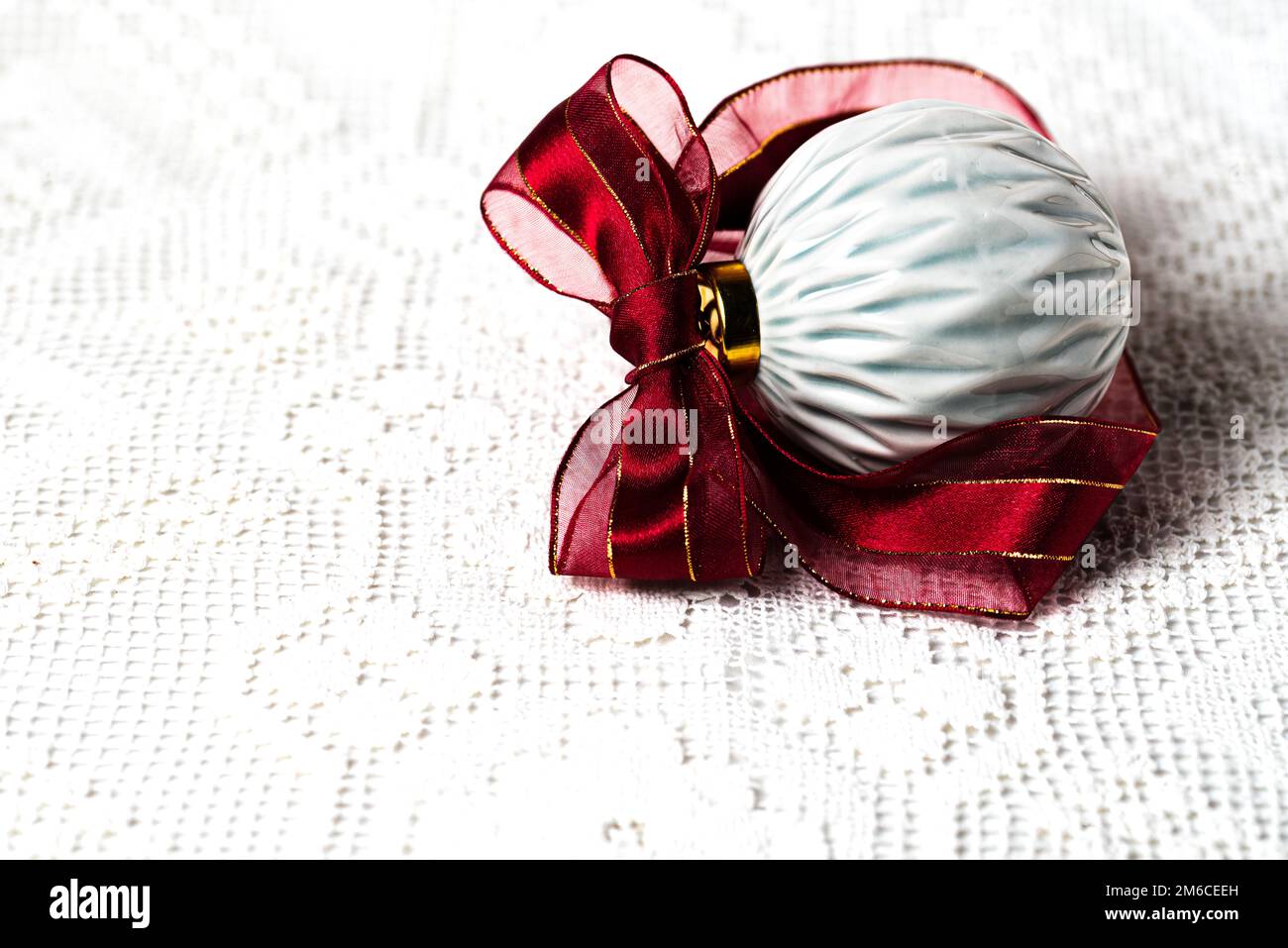 PALLA DI NATALE IN CERAMICA CON NASTRO BORGOGNA SU UNA TOVAGLIA IN PIZZO Foto Stock