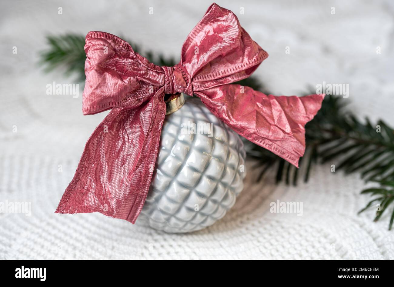 PALLA DI NATALE GRIGIA IN CERAMICA CON NASTRO ROSA SU UNA TOVAGLIA IN PIZZO Foto Stock
